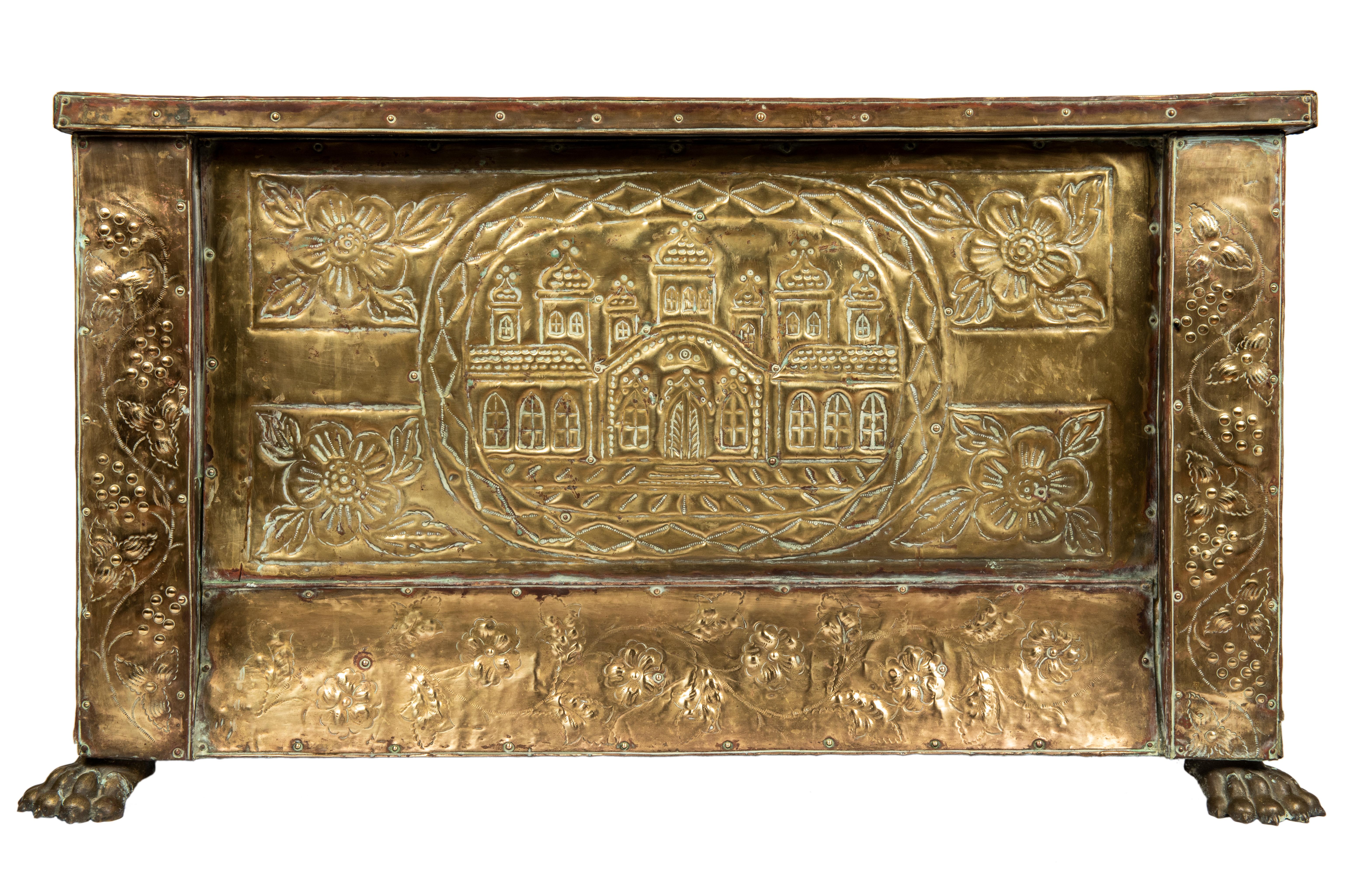 A rustic pine trunk adorned brass embossed panels, the front, sides and lid depicting flowers, vines, and berries, the hinged lid featuring a large Russian imperial eagle flanked by floral panels, the front, a church or monastery with onion domes,