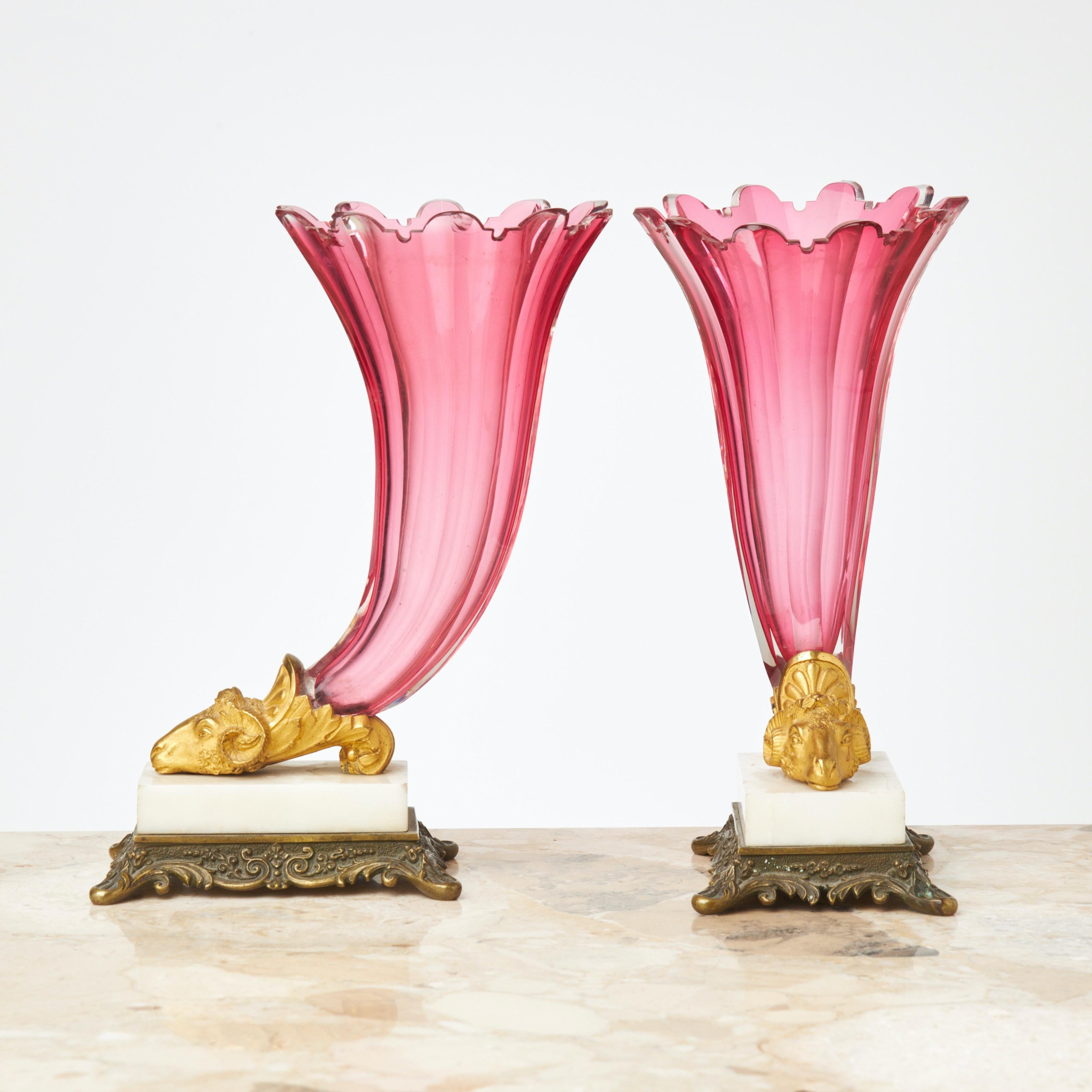 Una coppia molto decorativa di vasi Rython, detti anche Cornucopia, della prima metà del XIX secolo, probabilmente russi.  Vasi in vetro tagliato rosso/rosa con le estremità montate con teste di ariete in bronzo dorato che poggiano su basi in marmo