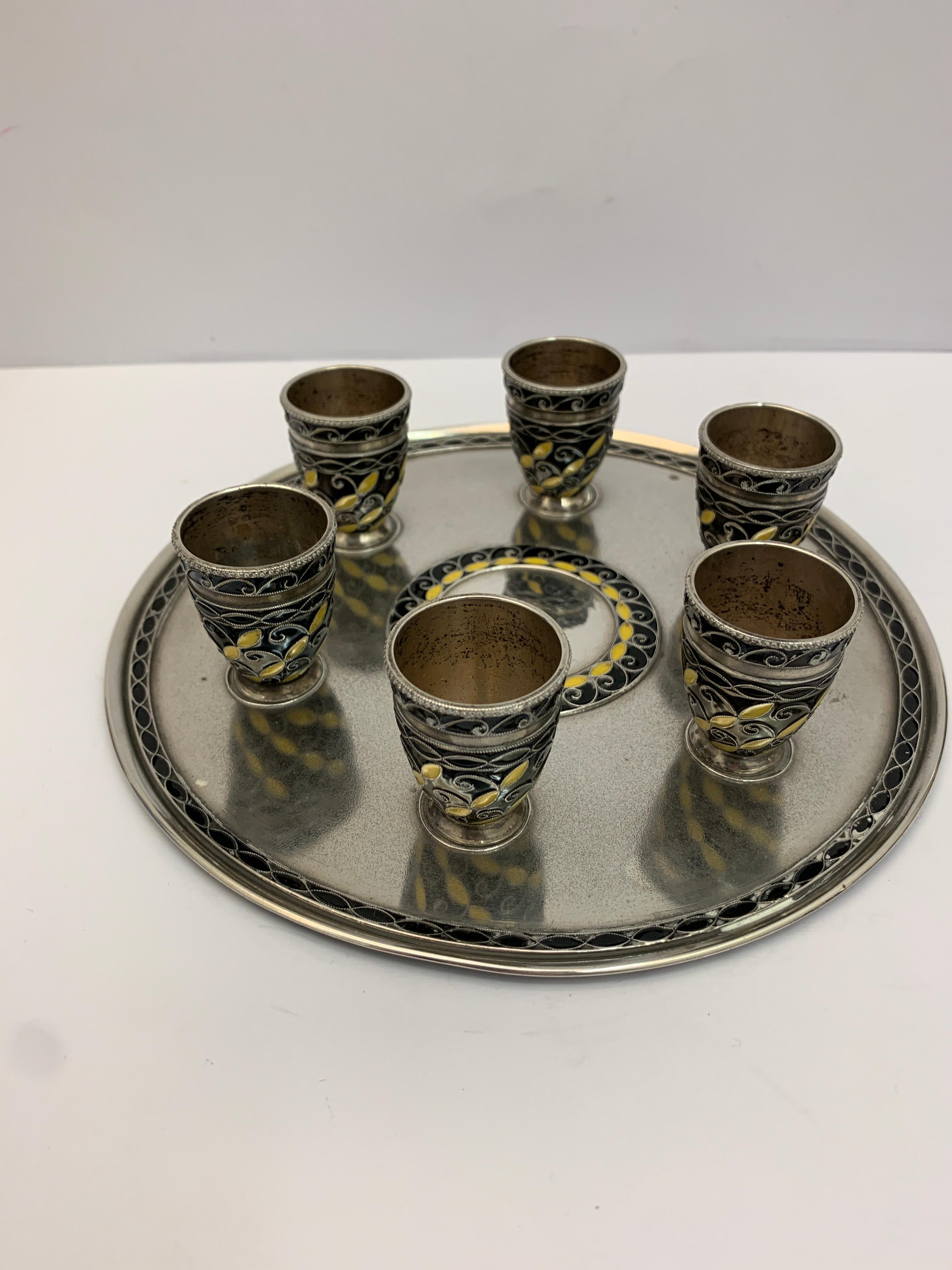A Russian silver and enamel drinking set, including 6 small drinking/shot tumblers and large silver ewer. All intricately decorated upon a circular silver tray.