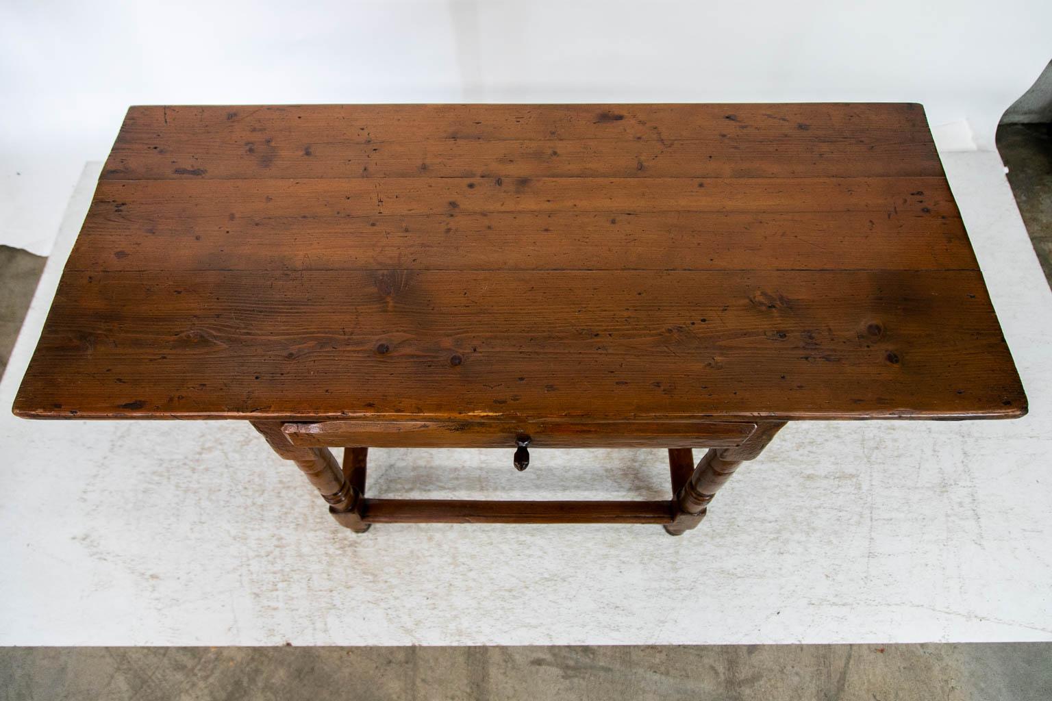 This pine tavern table has a wide overhanging top. The drawer has the original hand carved knob and applied drawer front. The base of the table has the original paint that matches the color of the natural finished top. There is exposed double peg