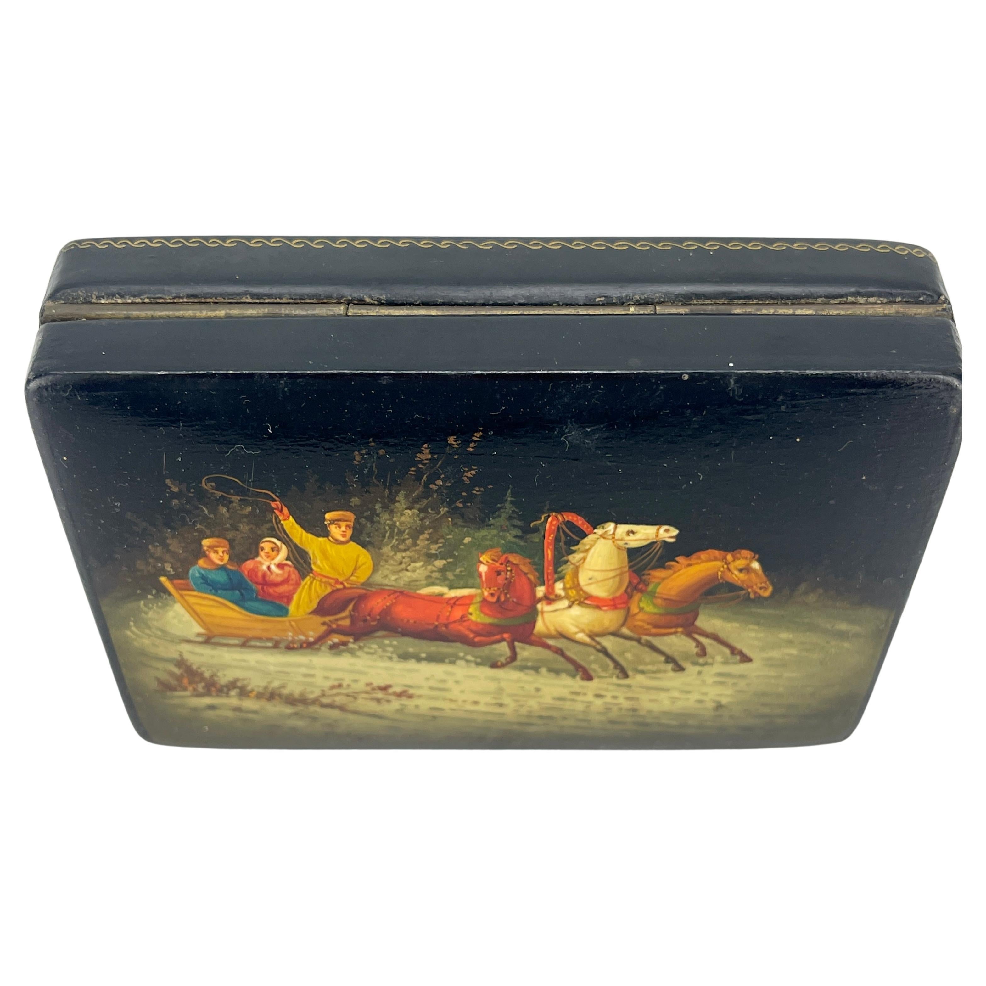 Rectangular Black and Red Lacquered Snuff Box, Signed and Dated 1971.
This tobacco snuff box is richly and colorfully decorated with a winter scene showing 3 people riding a sleigh in the snow being pulled by 3 wild horses.
This Soviet-era box has a