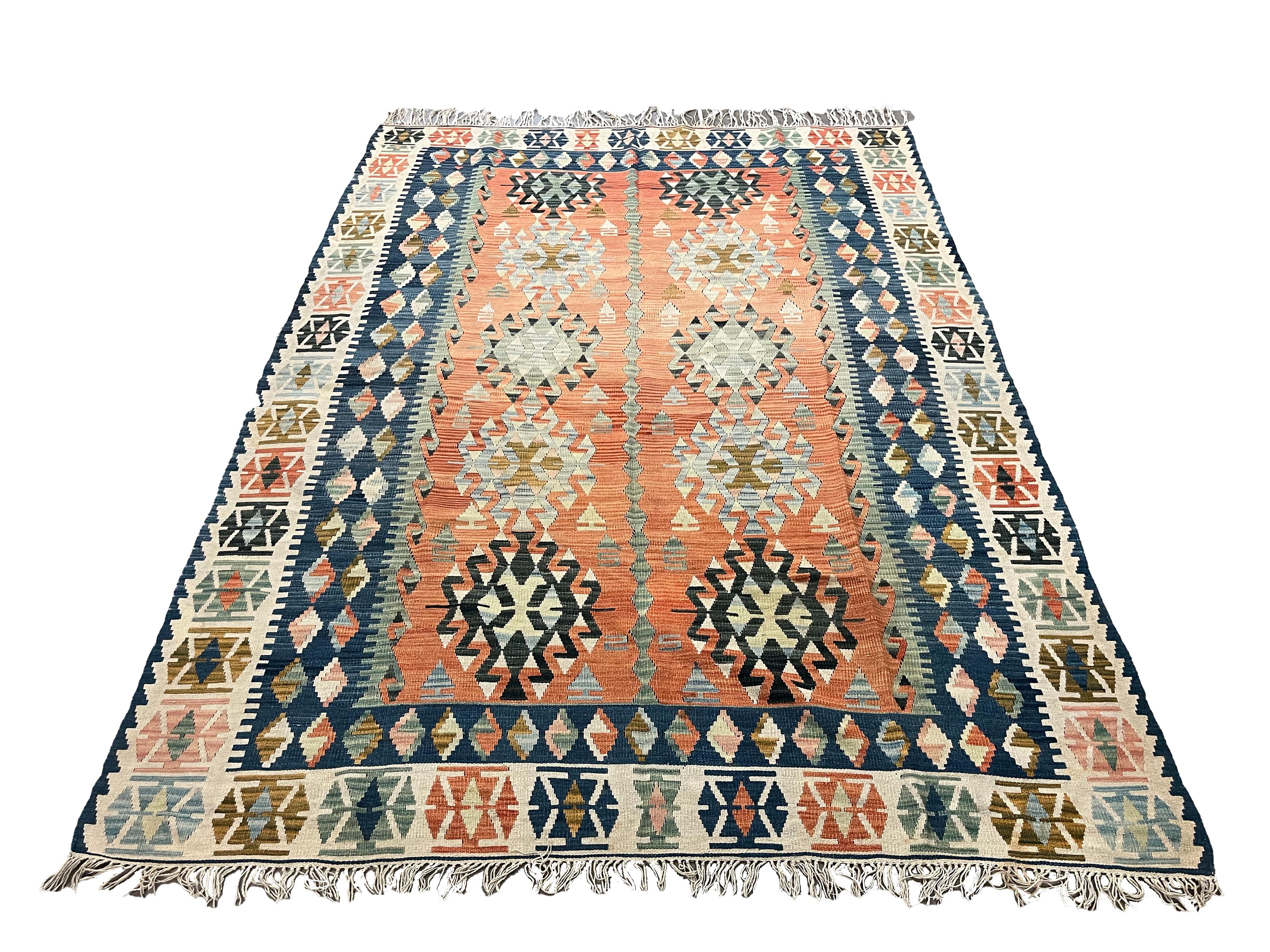 This bold handwoven kilim rug is an excellent example of a flatwoven geometric rug woven in Turkey in the early 20th century, circa 1910. The design features a bold geometric pattern woven in blue, beige, and brown accents on a bold rust background.