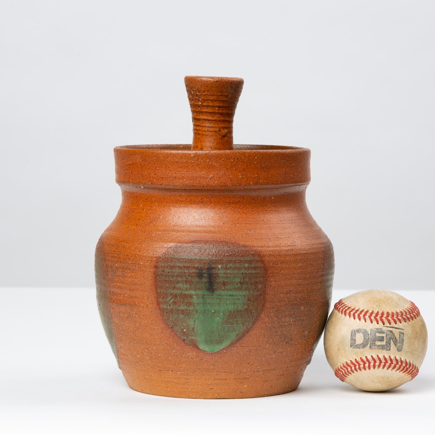A wheel thrown ceramic jar with pleasingly rounded sides and a lid in a rust red glaze. The handle of the jar is turned as well. Slightly raised spots in a green drip glaze adorn each pole of the jar. Signed “Doc Nelson” on underside.

Condition: