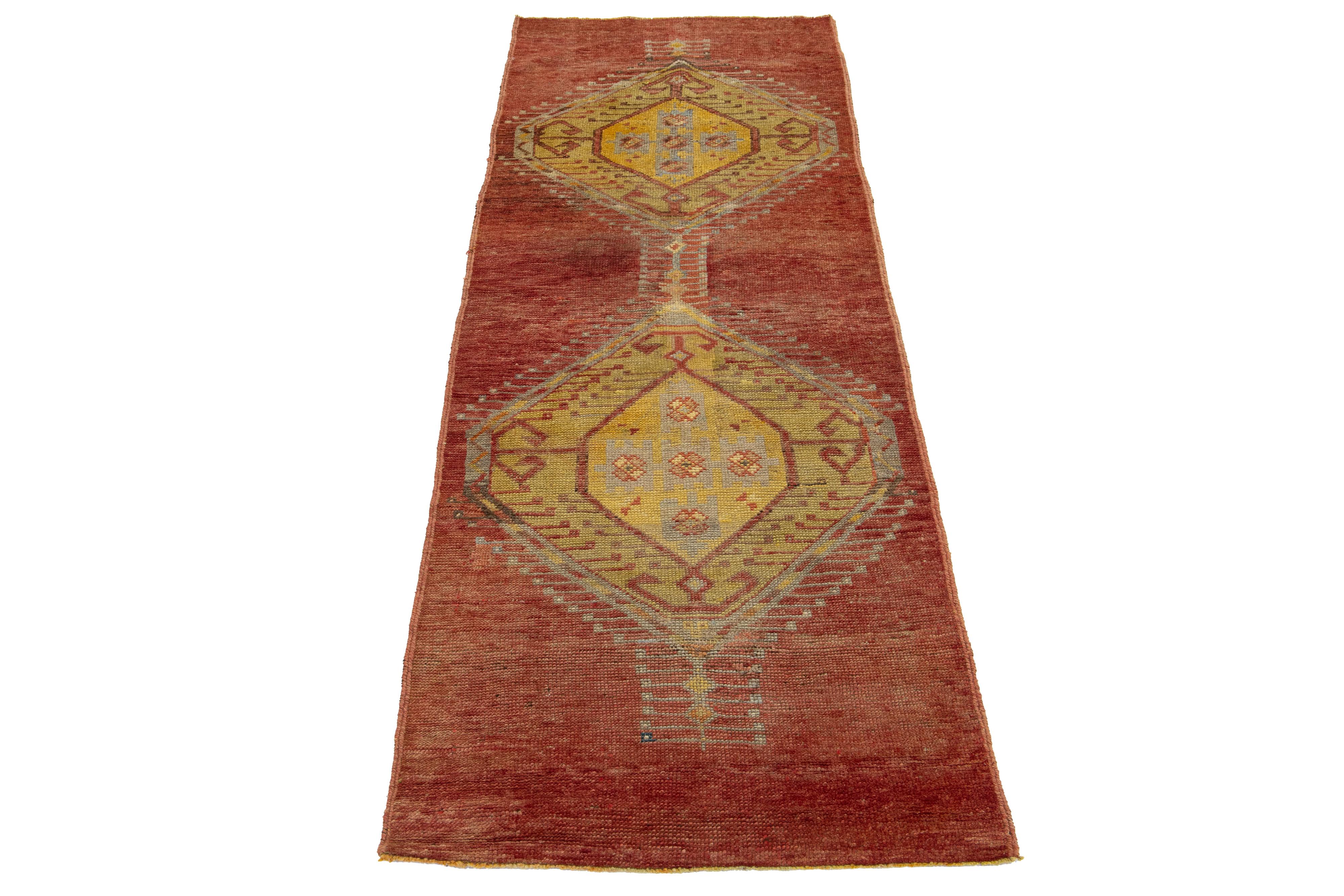 Dieser türkische Läufer im Vintage-Stil besticht durch sein auffälliges rostrotes Feld, das durch ein kompliziertes geometrisches Stammesmuster, das sich anmutig über den gesamten Teppich erstreckt, wunderbar ergänzt wird. Kräftige gelbe Akzente