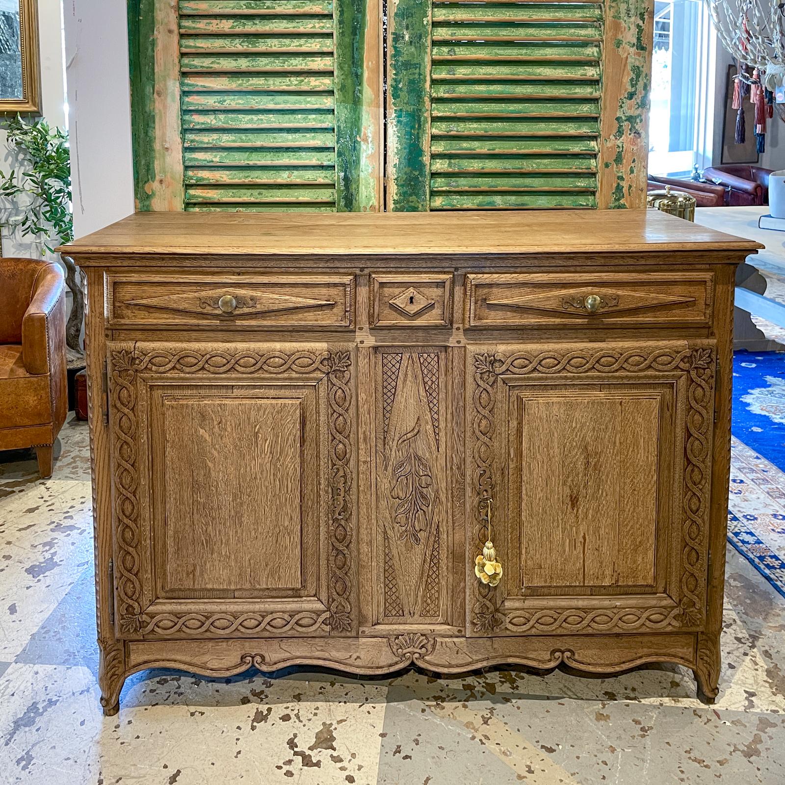 This antique French buffet is crafted in oak with three drawers and a lower cabinet with two doors. The front of the buffet has a number of carved details, including the shell at the center of the apron between the front legs. Between the doors is a
