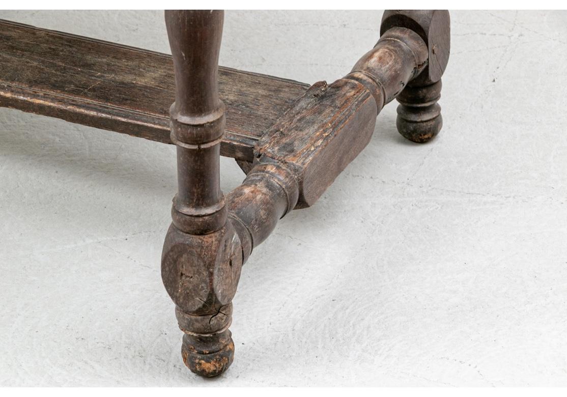 An authentic and Rustic oak console table in all original condition, likely English. In a dark stain with a plank constructed top with bread board ends. The Console Table has an interesting carved scalloped frieze on the front and back. The ends