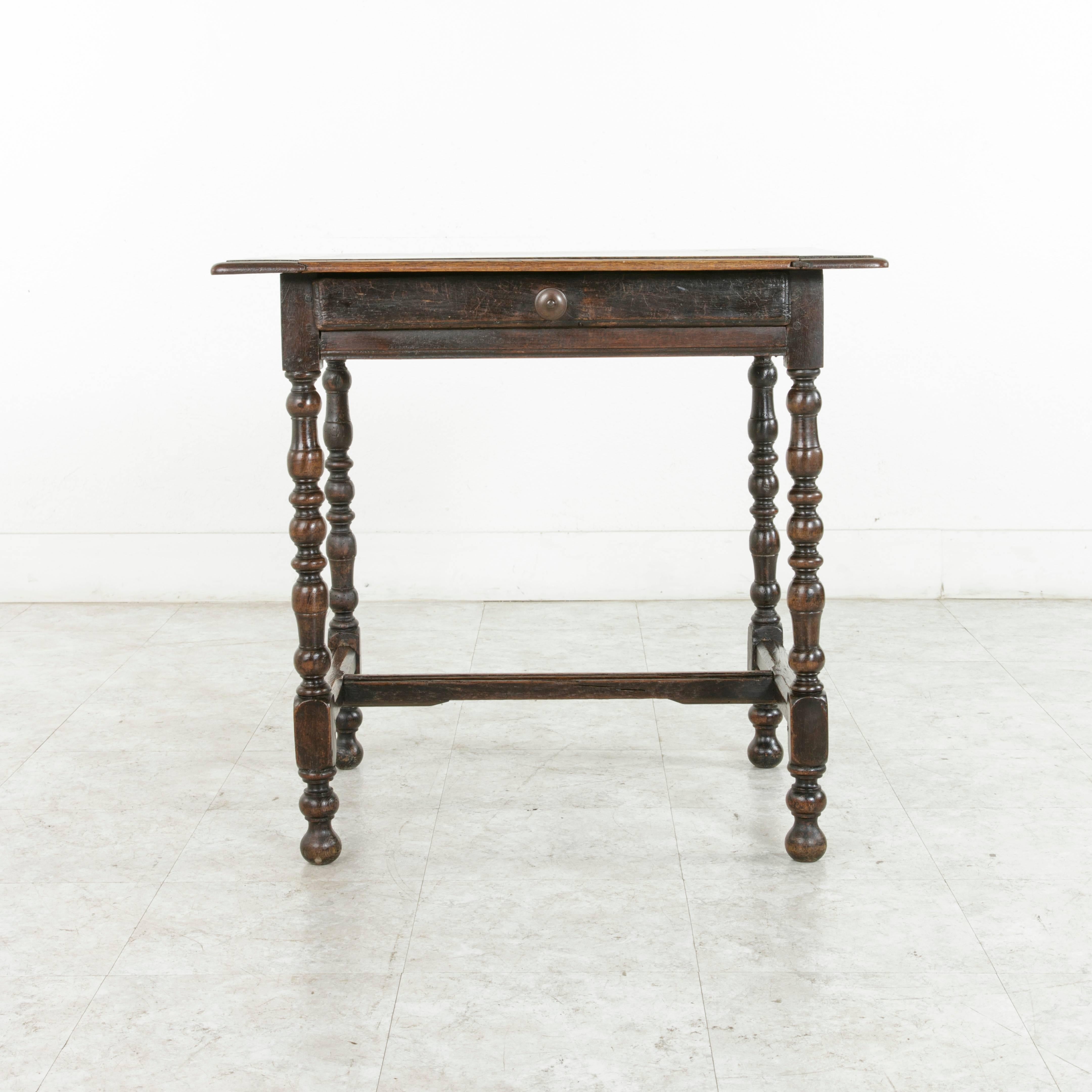 This French Louis XIII style oak side table or end table features an 18th century base supporting a hand pegged bevelled oak top fashioned in the 19th century. A single drawer of dovetail construction with an iron drawer pull between the hand pegged