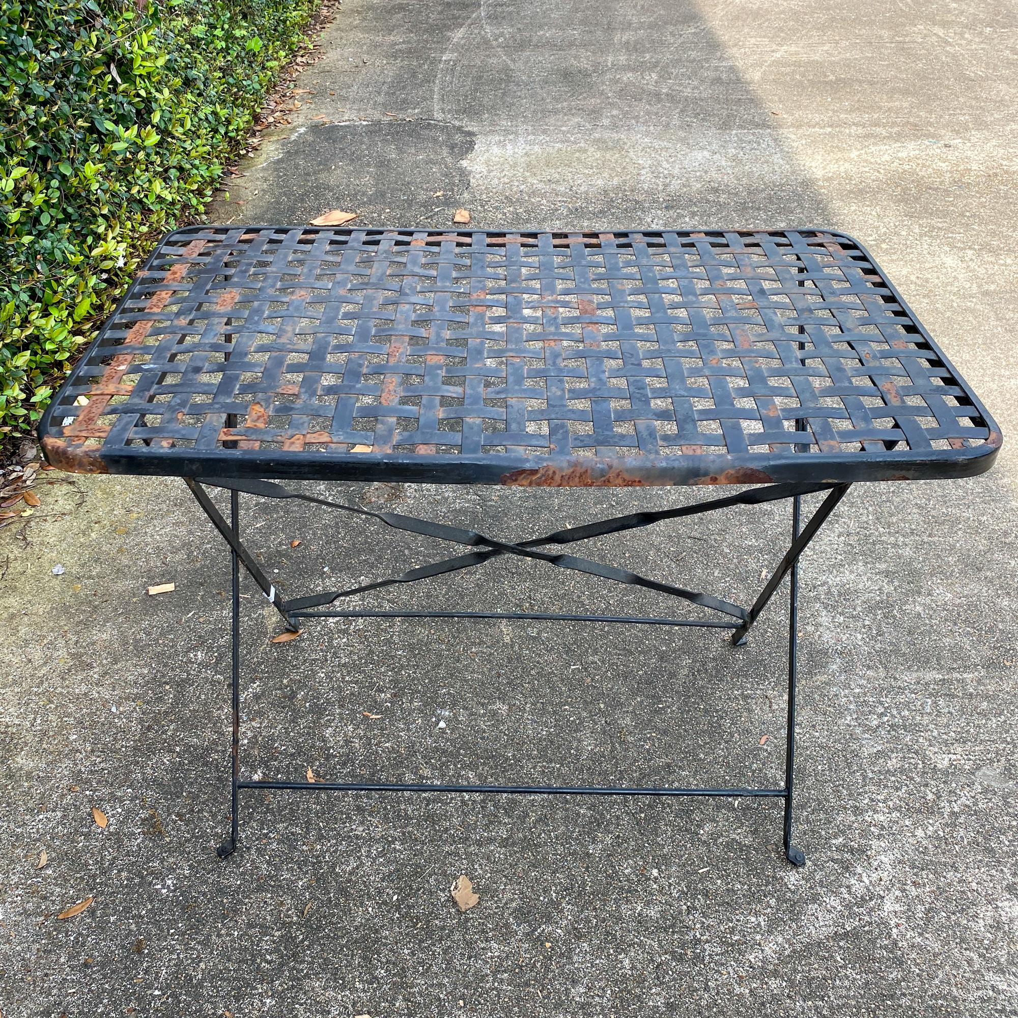 This is a 1940s wrought iron folding table sourced in France. The top has a woven look and the corners are rounded, with a beautiful patina. The legs are sturdy and feature a locking mechanism for stability. The legs also have a decorative twist in