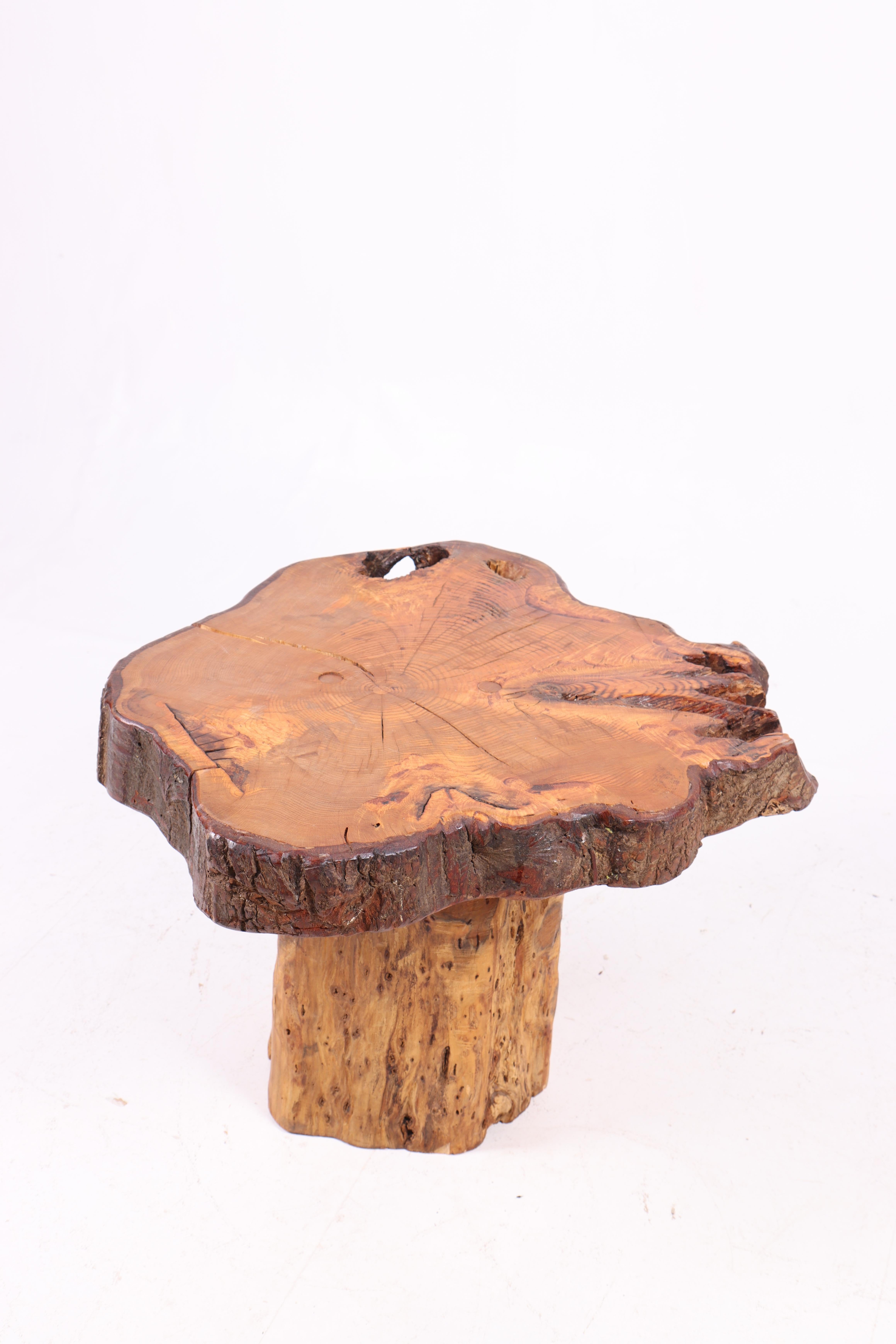 This coffee table from the 1950s is crafted from solid elm wood and features a unique, organic design. The tabletop is cut from a large slice of elm, giving it a rustic and natural feel. The surface texture showcases the wood's grain and structure,