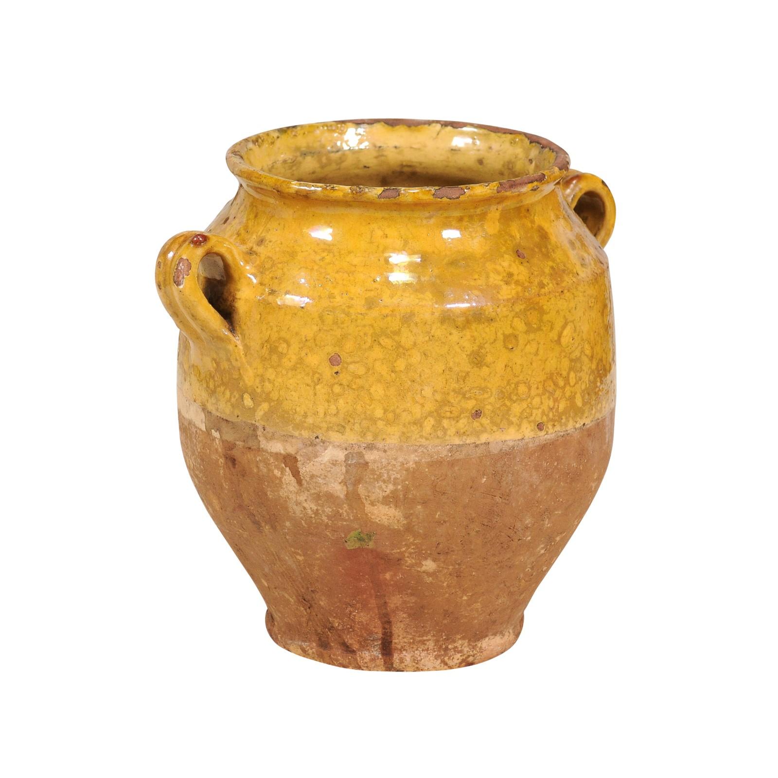A rustic French Provincial pot à confit from the 19th century with yellow glaze and double handles. Immerse yourself in the rustic allure of this 19th-century French Provincial pot à confit, a piece that embodies the essence of rural French charm.