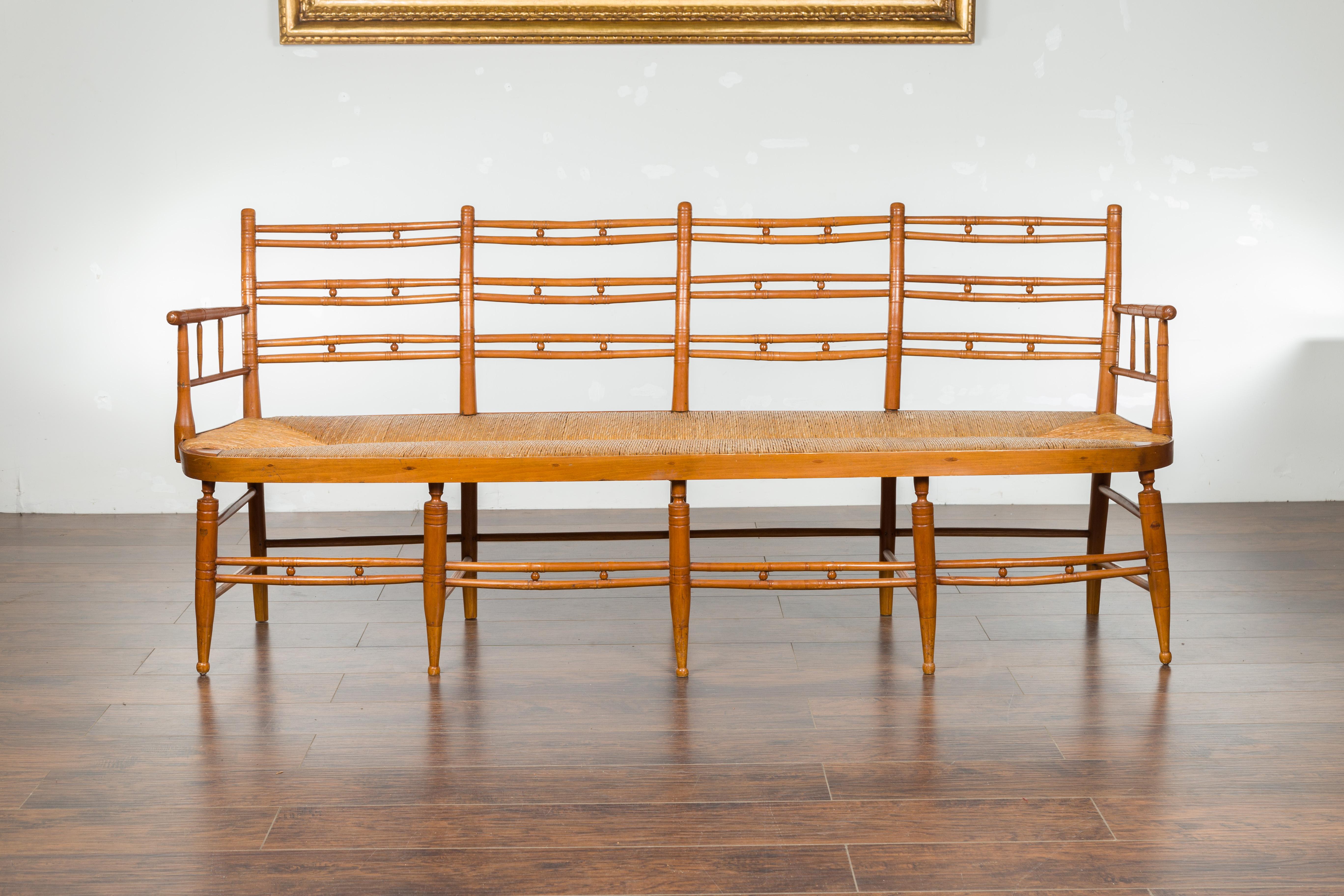 A rustic French walnut bench from the 19th century, with open back and rush seat. Created in France during the 19th century, this walnut bench features a slightly out-curving back with pierced accents, connected to two arms flanking a long