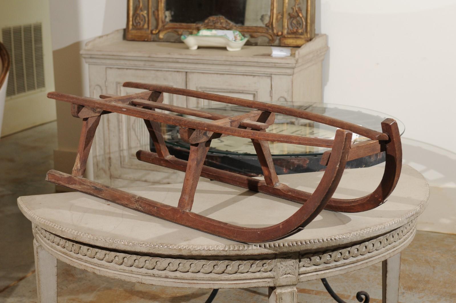 A French rustic wooden sled from the 19th century with curving extremities. Charming our eyes with its rustic appearance and nicely weathered patina, this French sled is made of simple wooden slats resting on trestles raised on a curving base, ideal