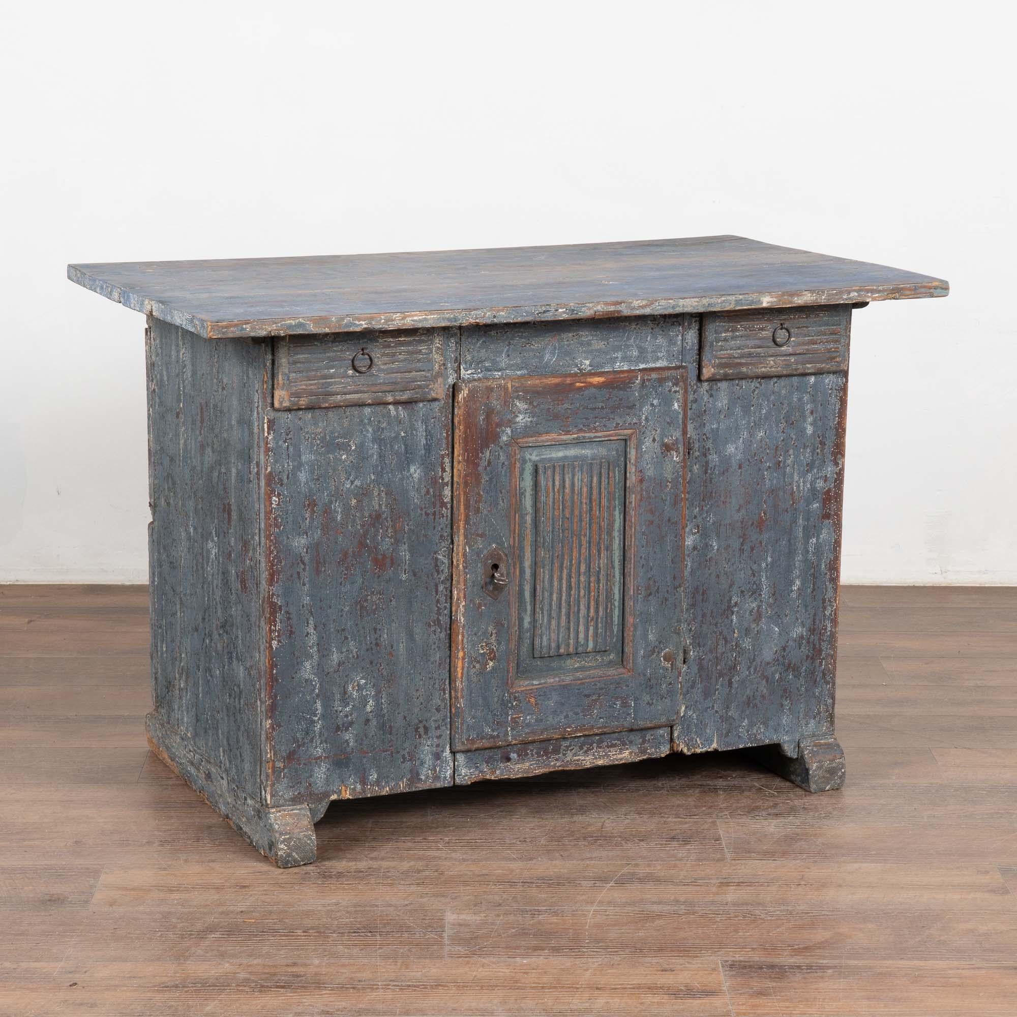 Antico mobile o piccola credenza in pino svedese con due piccoli cassetti sopra un'anta.
La finitura originale dipinta di blu (con sfumature bianche e grigie) è stata rovinata nel corso di molte generazioni, rivelando la calda patina di pino