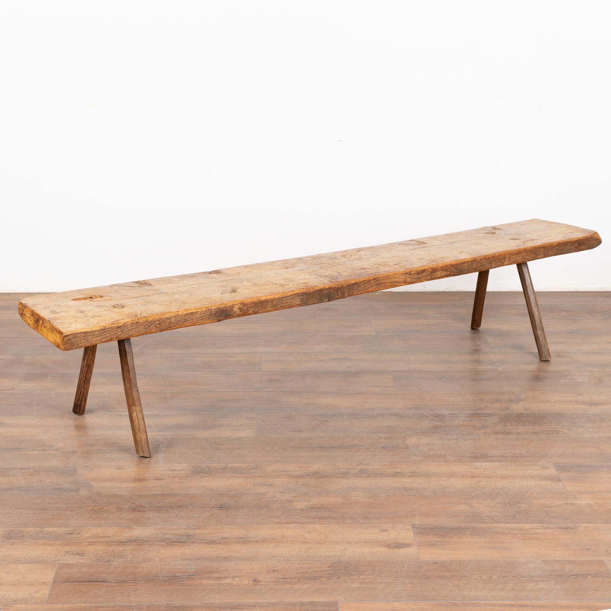 Rustic plank top bench with splay peg legs over 6' long.
The top reveals generations of use with cracks, nicks, stains and old dried worm holes which add character to the narrow bench.
Restored and waxed, this bench is strong, stable and ready for