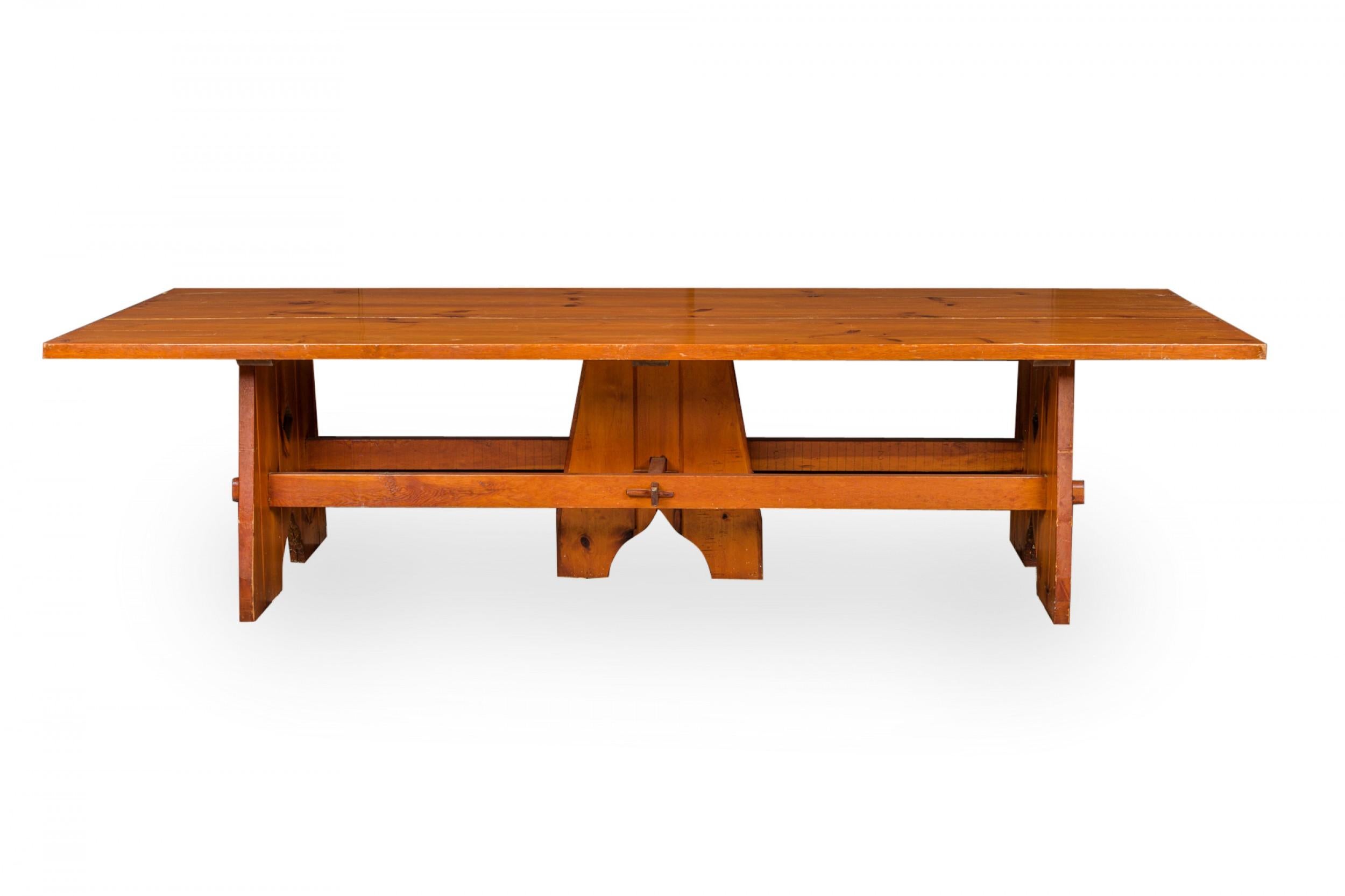 Rustic Adirondack-style (Mid-20th Century) large stained and sealed pine wood dining table with a rectangular plank wood top resting on a base comprised of three wide legs with a stretcher base and tusk and tenon joinery.