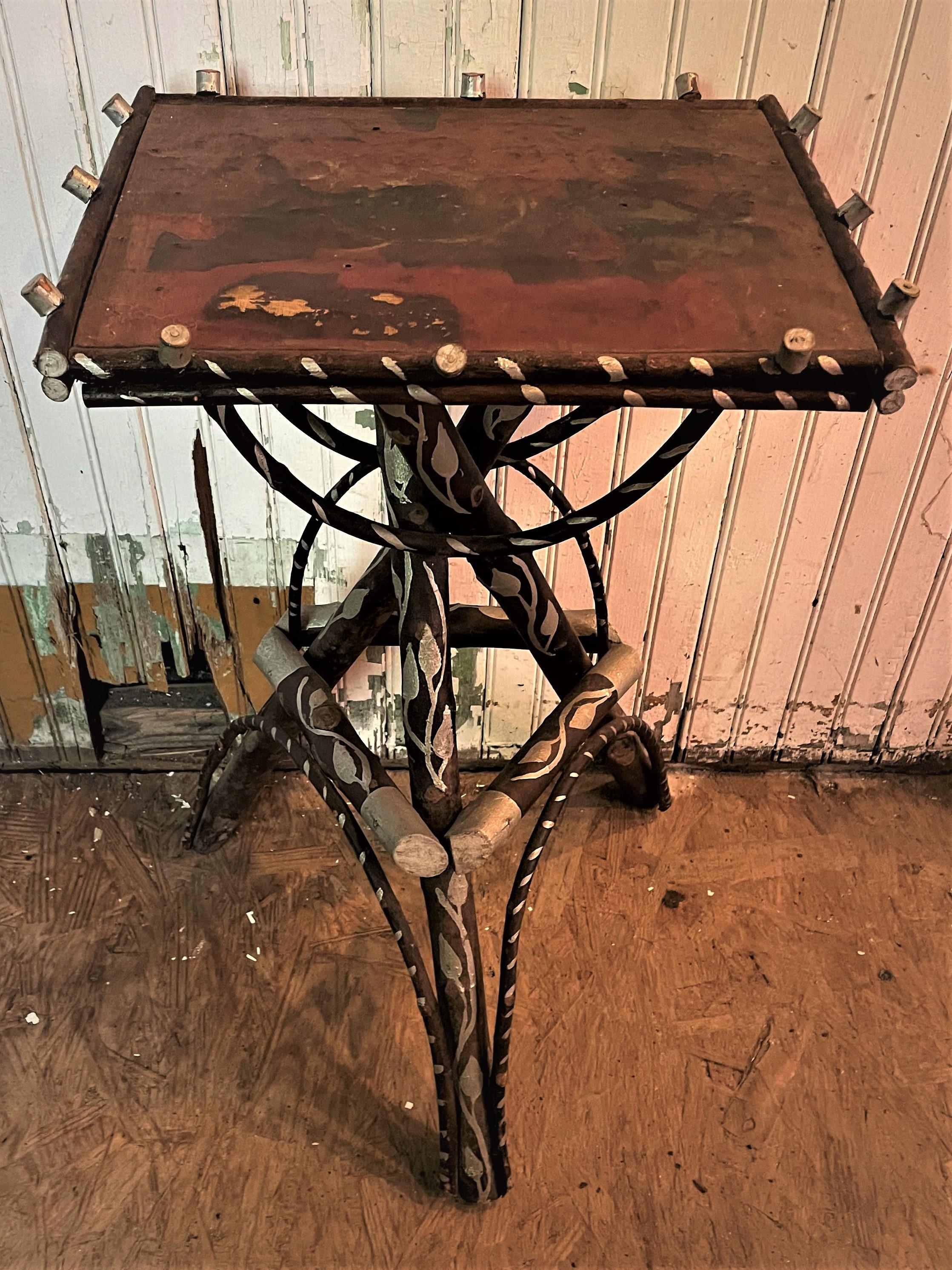 This is the sweetest Adirondack stand or side table with a dark finish decorated with silver paint and an aged brick red finish on the top. The base has a vine and end caps on all the wood and cross hatching on the bent twigs painted in silver