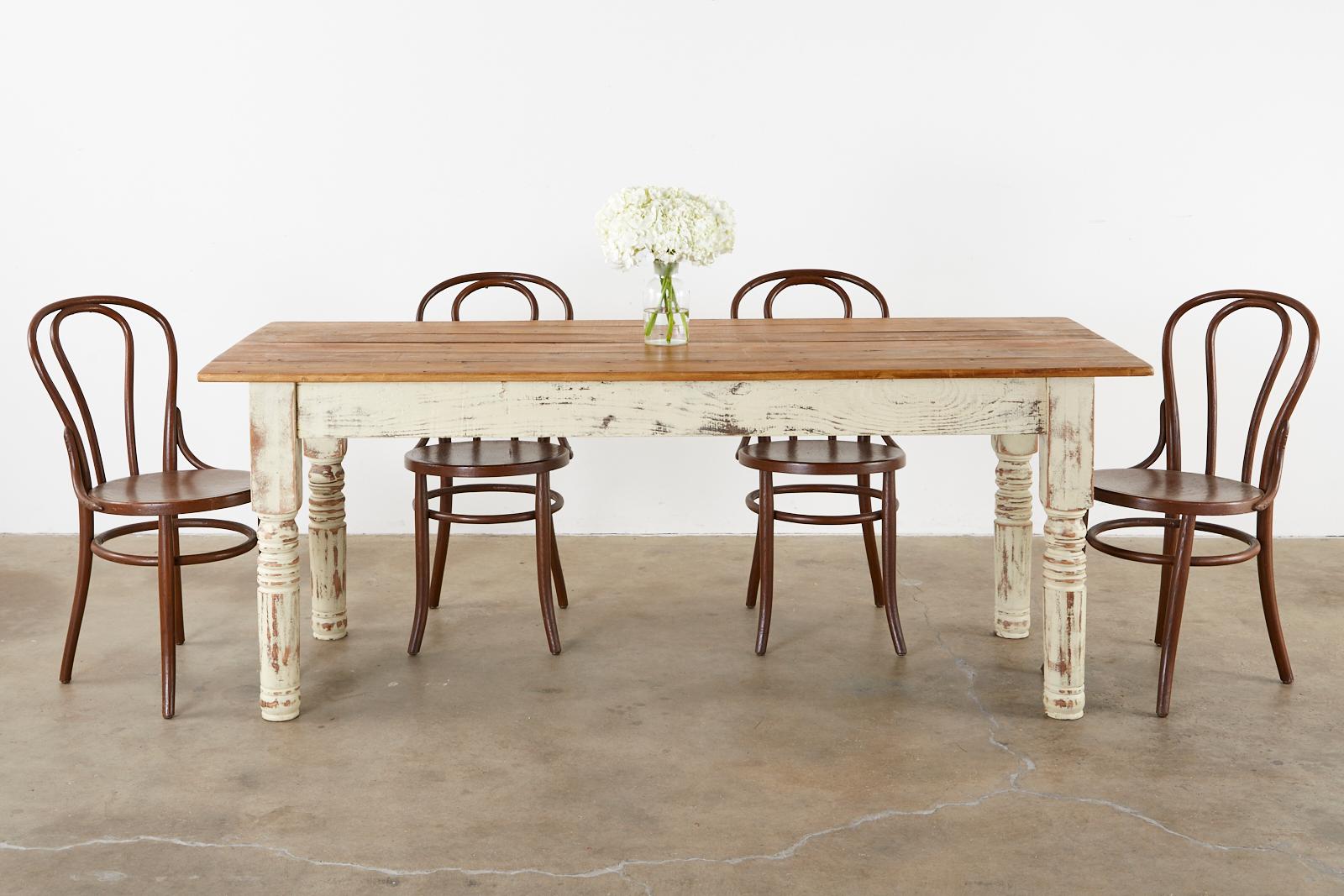 Country American rustic farmhouse dining table or harvest table featuring a cream colored painted pine base. The top is constructed using reclaimed pine barnwood with tongue in groove joinery and a natural finish. Old fence nail holes are still