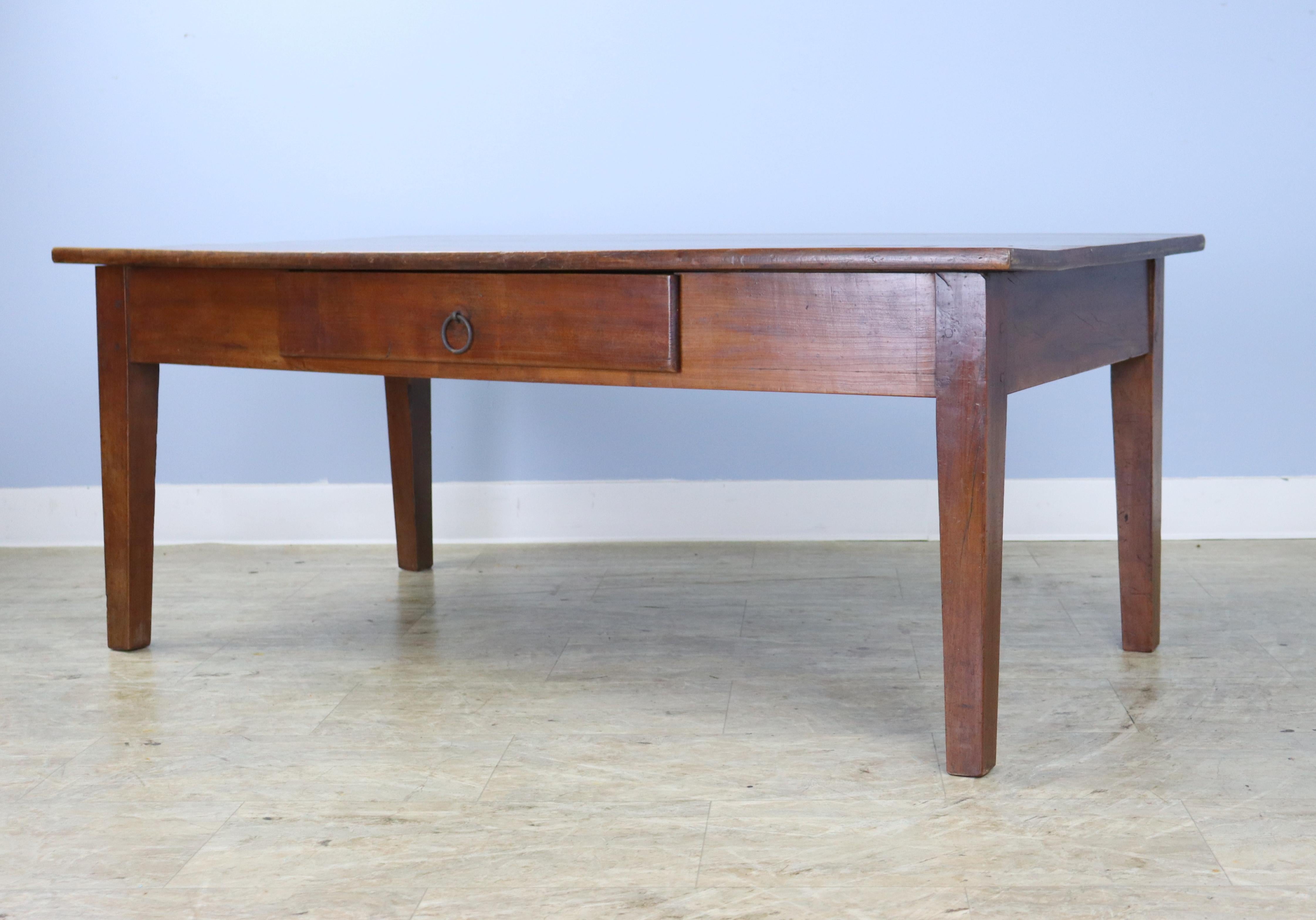 A sturdy and handsome cherry coffee table, with a thick chunky top and a single drawer for storage and visual interest. Slim wrought iron ring lends a rustic look. The cherry has great grain and patina, though there are some ring marks and stains.