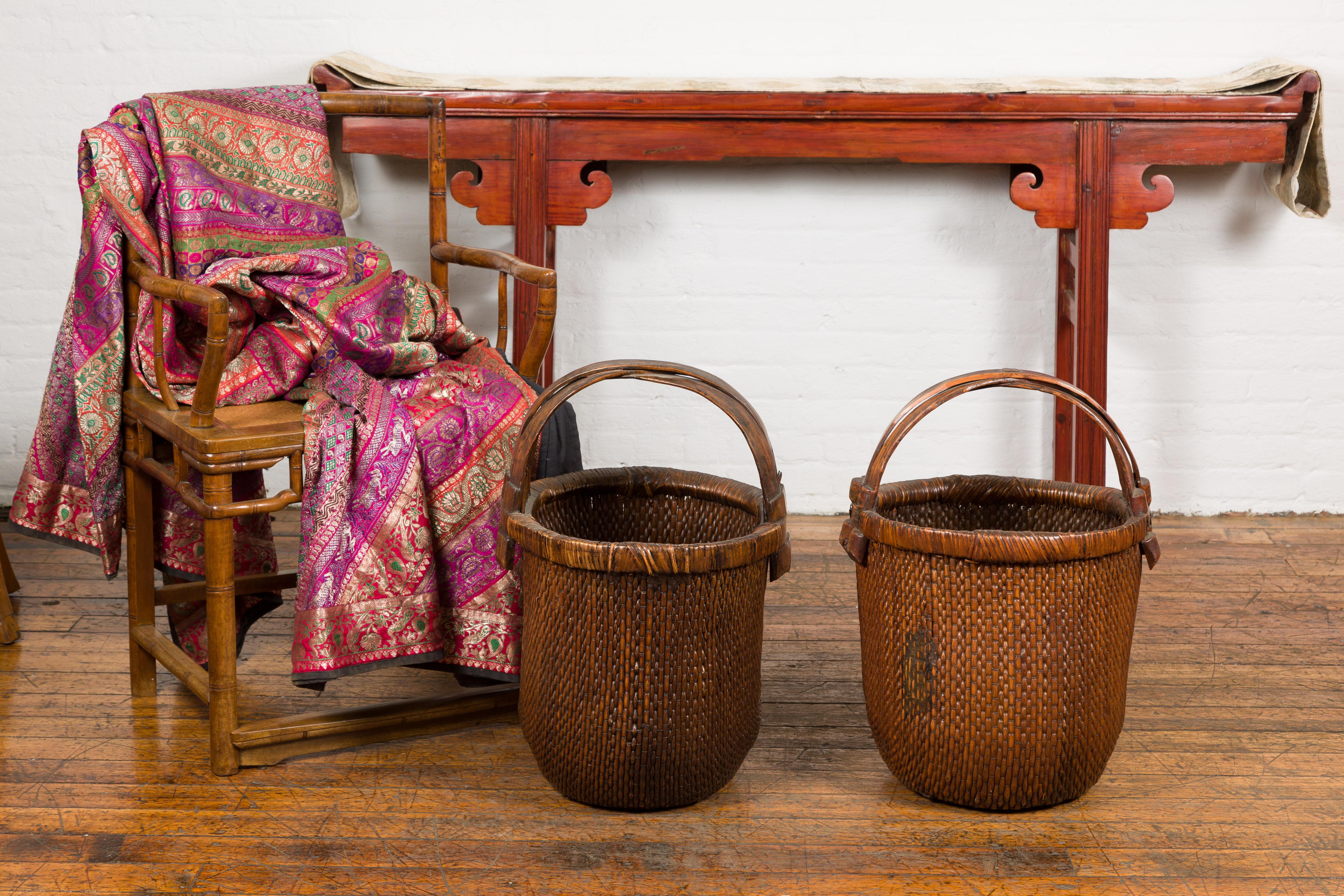Two willow grain baskets with wooden handles and rustic character. Embrace the rustic charm and rich history with these two Chinese antique willow grain baskets, which are the epitome of pastoral elegance. Over 60 years old, these baskets, with