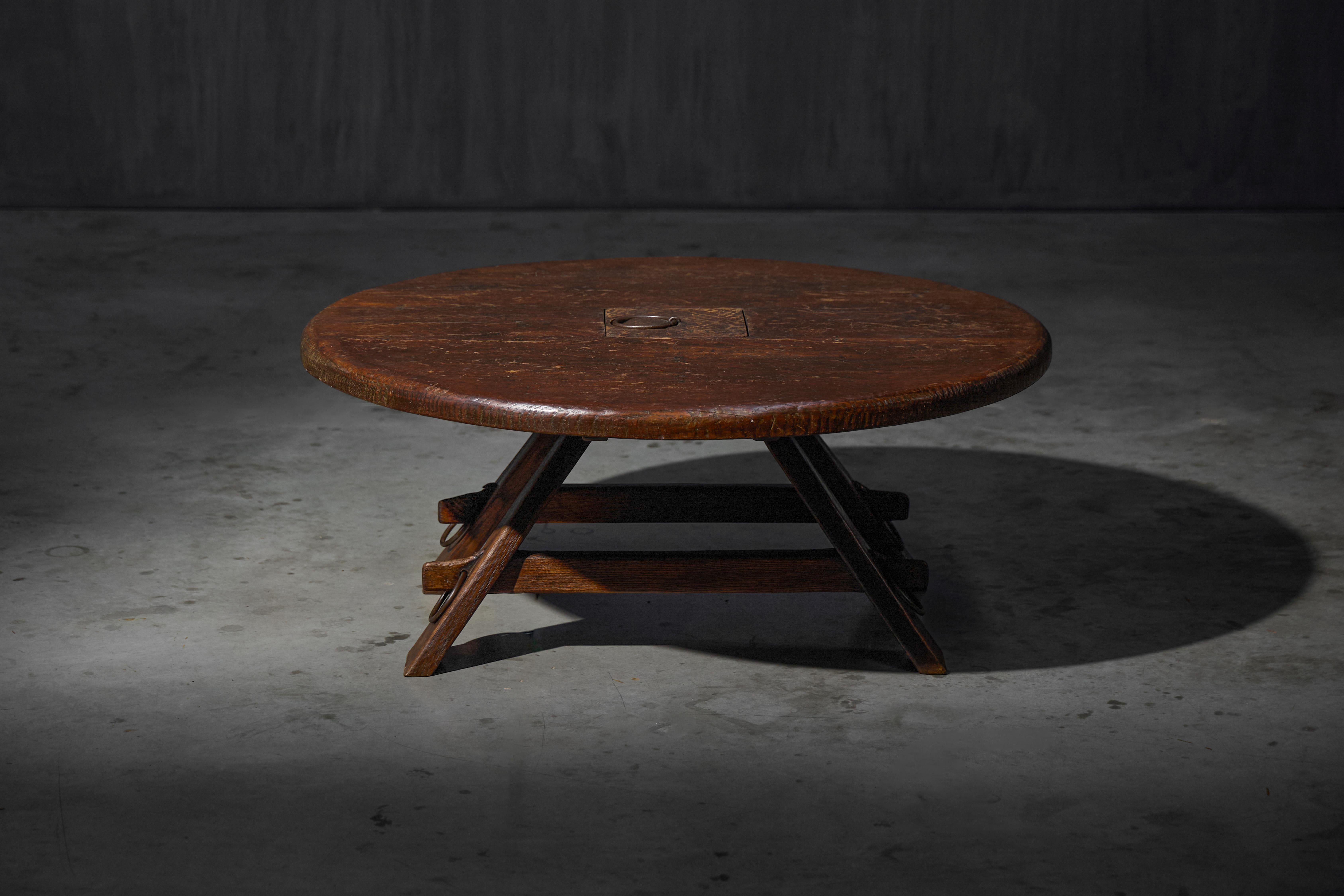 Fabricada en madera oscura, esta mesa de centro de perfil bajo tiene un diseño sencillo y robusto. El anillo central y las patas en ángulo le dan un aspecto ligeramente industrial y brutalista. Los signos de desgaste añaden carácter y muestran su