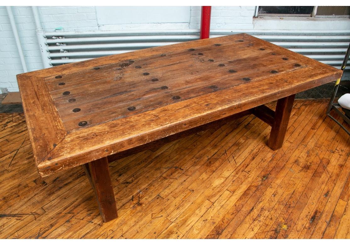 The large and very well constructed rustic table made up of an antique door with plank construction having wide outer banding and mounted with flat iron bosses in bands, and with a shaped iron lock. Raised on an antique wood base with square legs