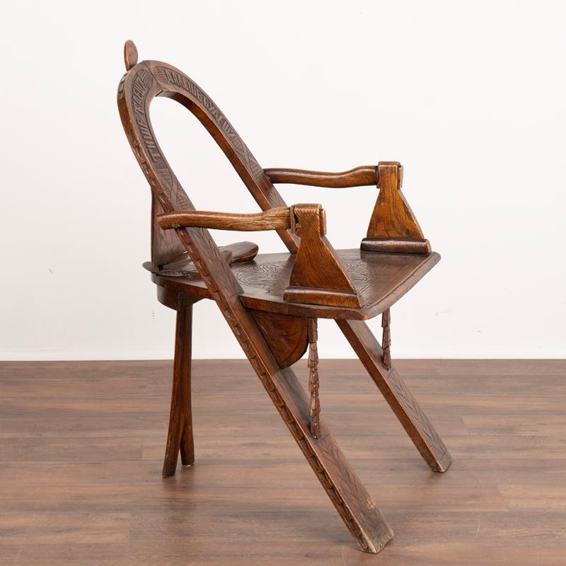 Dieser faszinierende rustikale Stuhl hat ein traditionelles dreibeiniges Design mit aufwendigen handgeschnitzten Details, einschließlich Schnitzereien entlang der Sitzfläche und Namen, die die Rückenlehne einrahmen. Bitte betrachten Sie die
