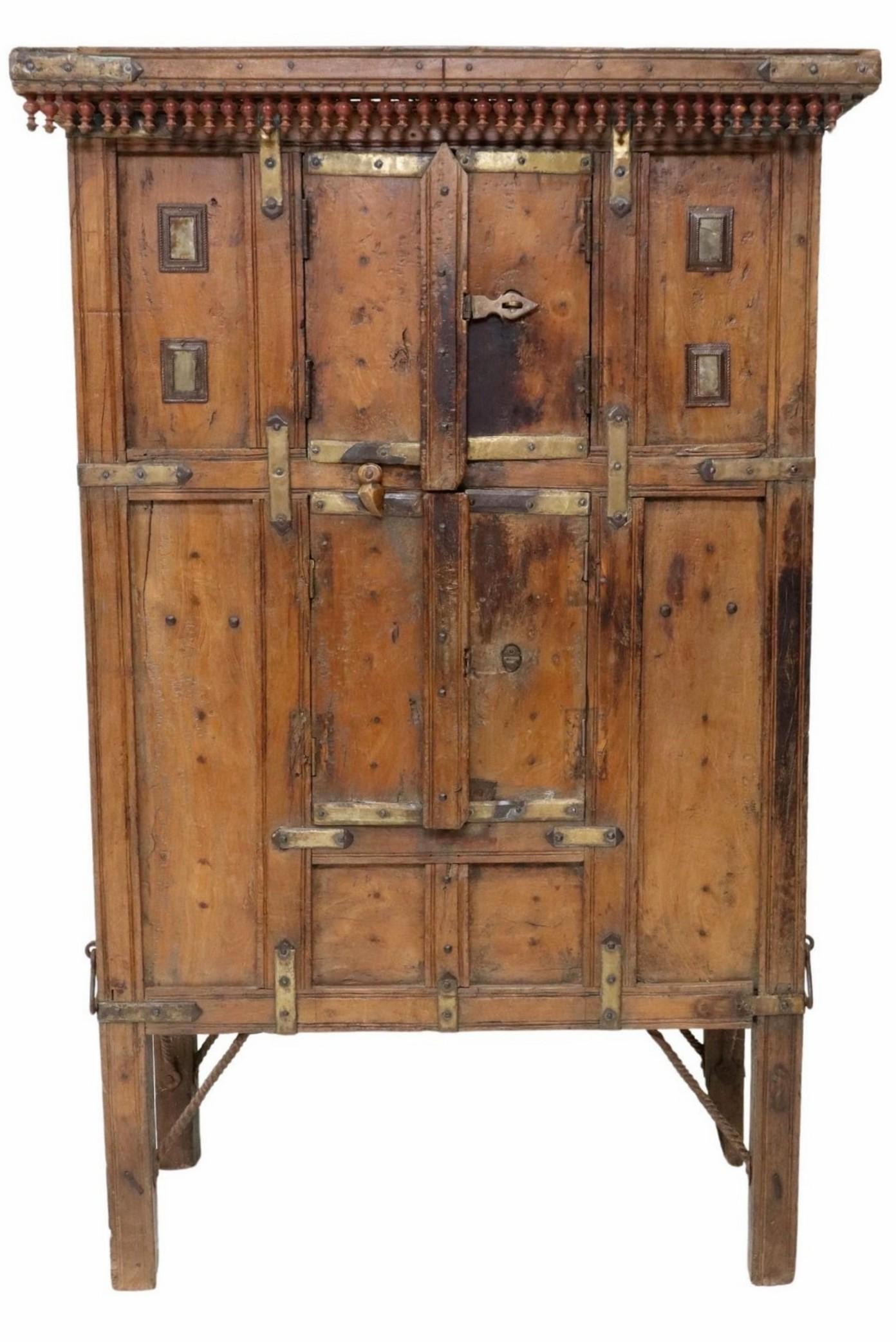 A rare and most impressive rustic Indian metal mounted spindled and carved wood cabinet. 

Hand-crafted in India in the 19th century, the one-of-a-kind folk art work features a rectangular cornice with drop spindle ornamentation, paneled heavy-duty