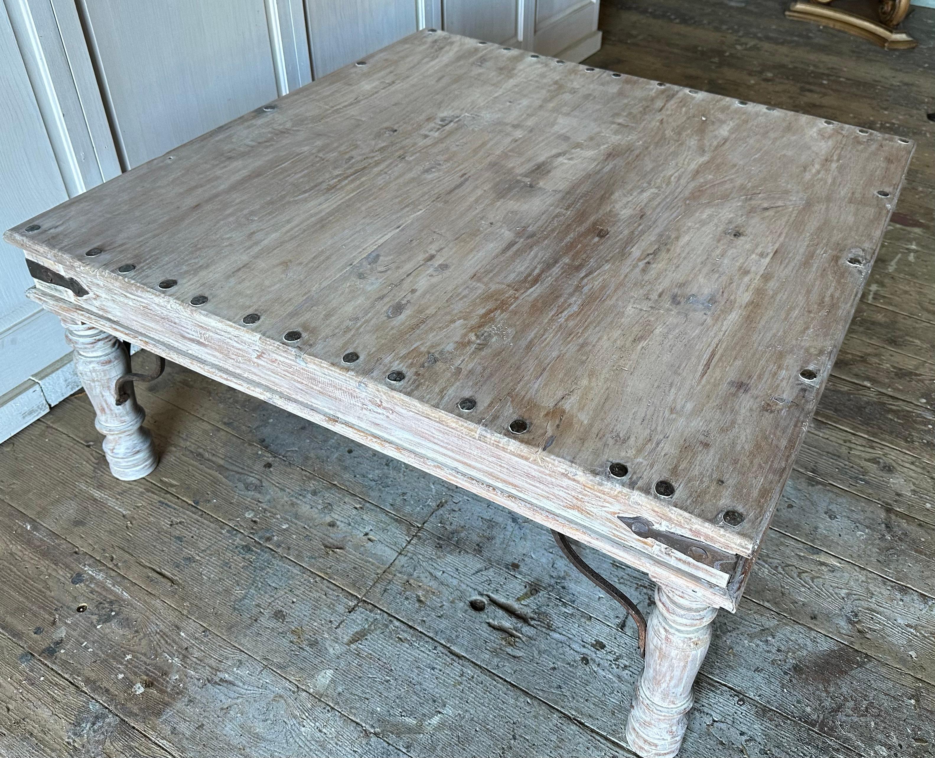 Antique 19th Century square coffee table created in India of sheesham wood. This coffee table is crafted with rectangular plank top accented with metal stud nailheads, resting on four turned baluster legs connected to an apron with iron corner