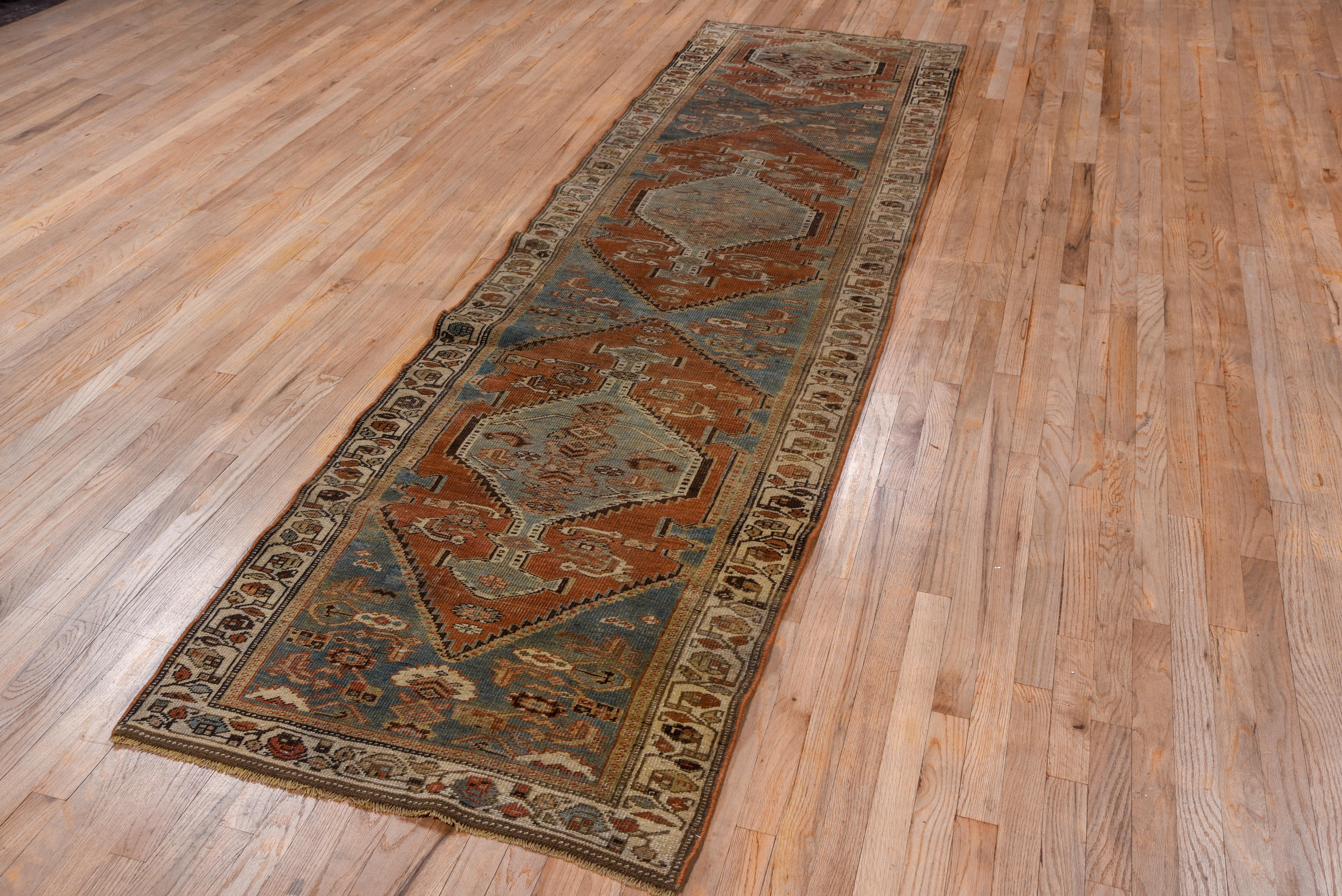 A NW Persian village runner creation, nearly three complete red hexagonal panels display pale green pendanted medallions with light blue side filler triangles and scatters of flattened 'fish' leaves. The cream border features a tendril with round