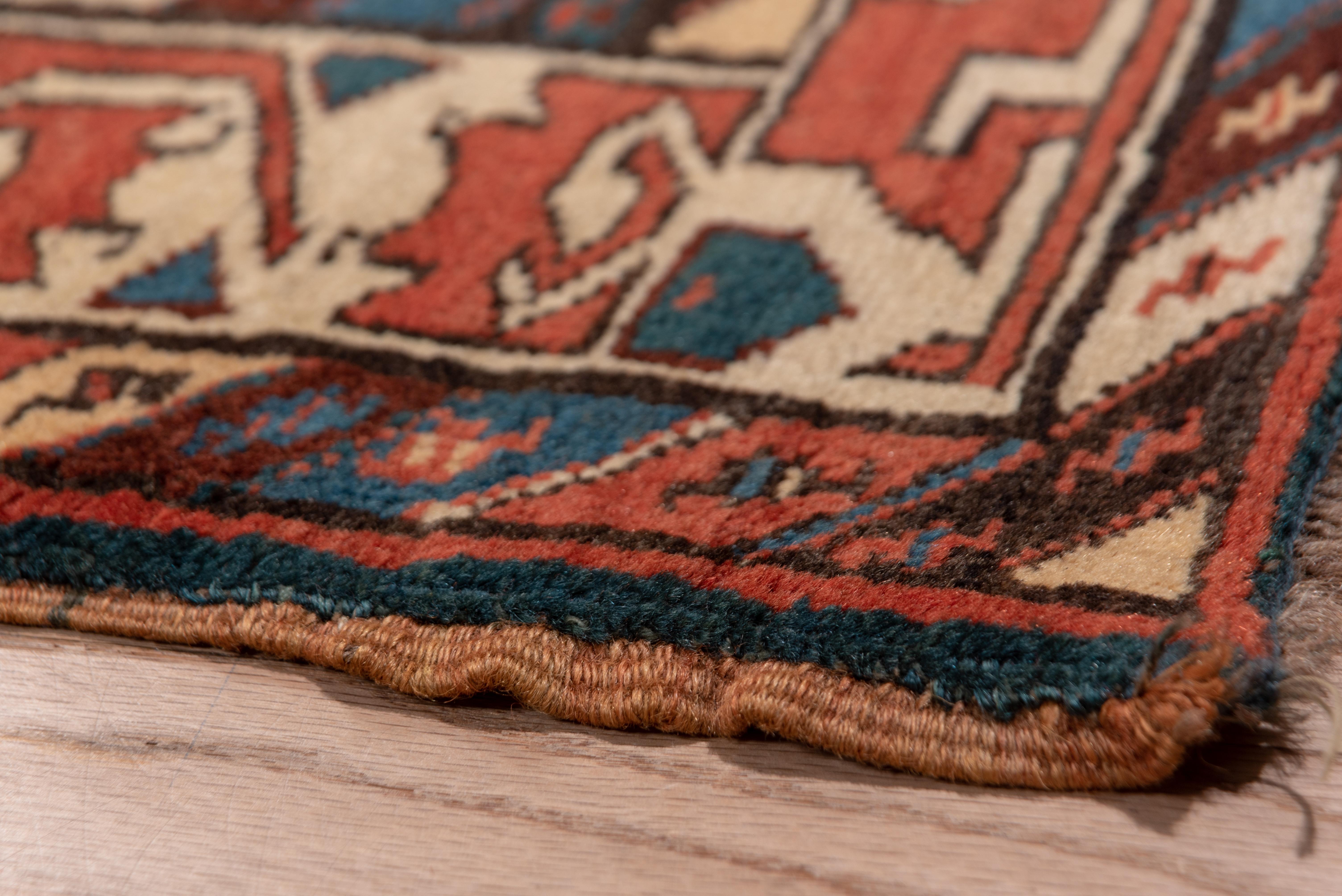 The red, blue and brown field of this rustic runner show tightly packed, reversing offset rows of hexagonal botehs accented in medium blue. The unusual Turkmen-style ivory strip-style border shows reversing paired serrated curled leavers forming