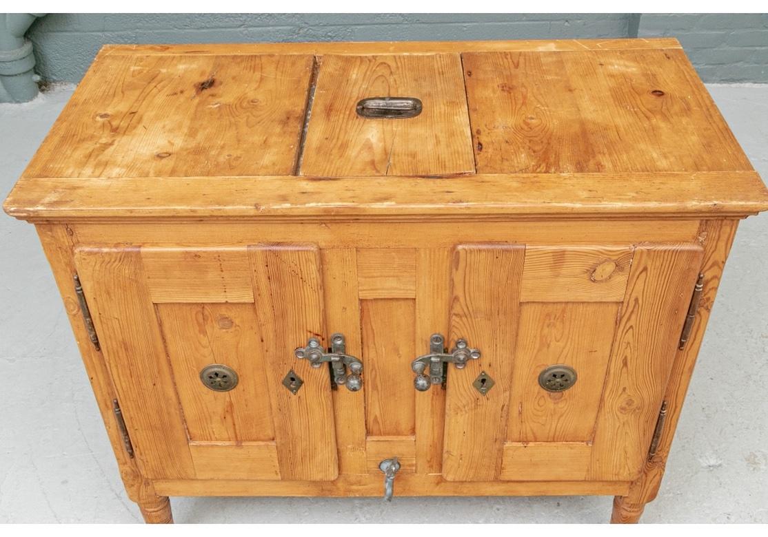 A well-constructed pine chest with a lift- up panel on top to reveal a tin lined removable bin. With double doors with iron mounts and a metal lined interior. Pierced roundels on the sides for ventilation. Raised on ring turned cylindrical legs in