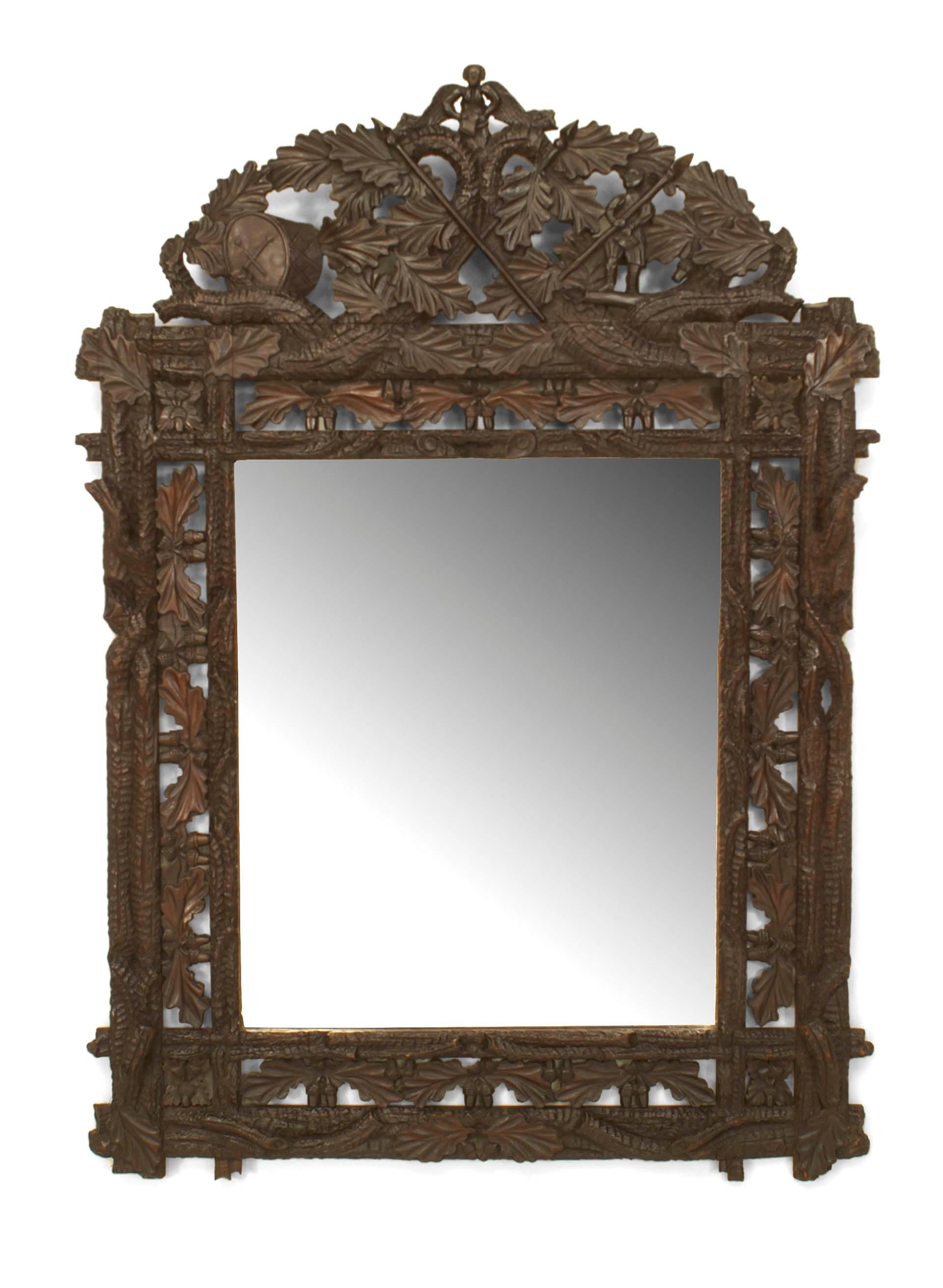 Rustic black forest carved wall mirror positioned within a filigreed faux twig and oak leaf design frame beneath a dramatic foliate pediment.