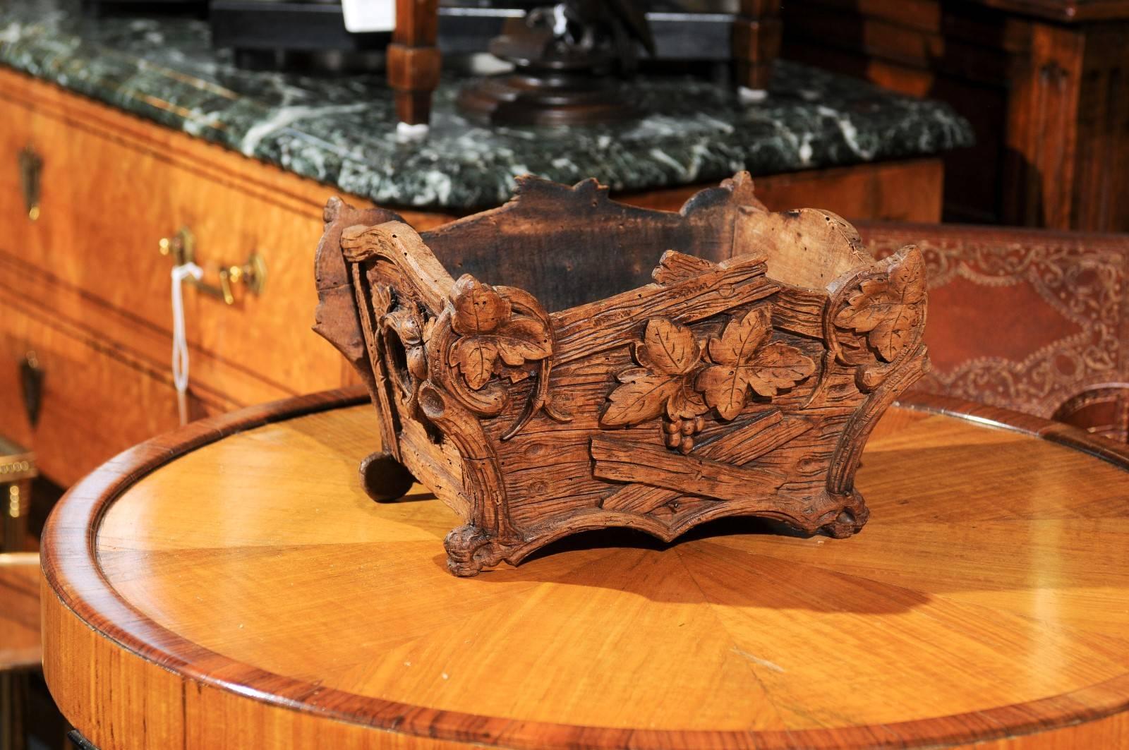A petite black forest carved wood jardinière from the early 20th century with foliage motifs. Featuring a slightly splayed structure, this exquisite small size jardinière is adorned with a décor of carved planks and foliage motifs on the surround