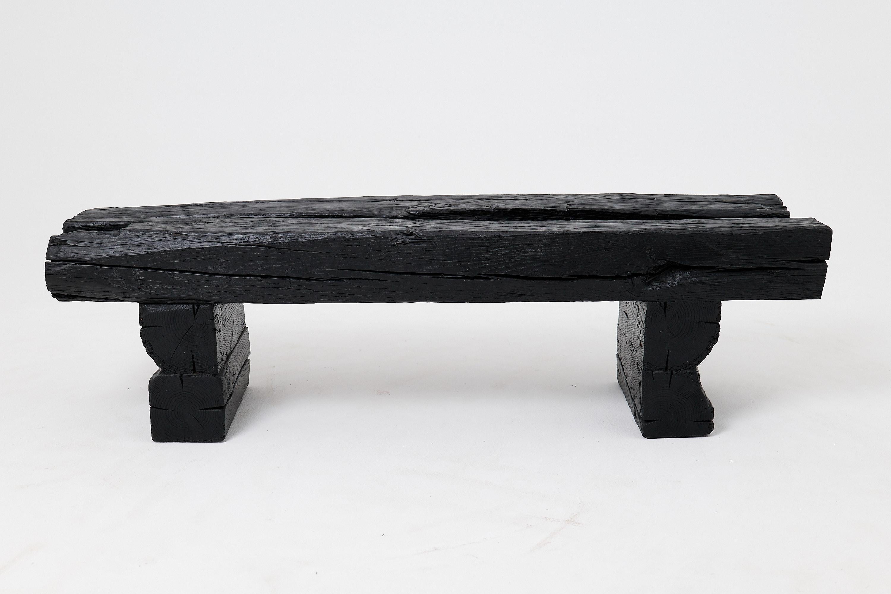 Ce banc monolithique est une pièce unique, fabriquée à partir de poutres massives en chêne récupéré, vieilles de plus d'un siècle. Sa forme puissante et minimaliste est unifiée par une finition ébénisée profonde, transformant le bois ancien en une