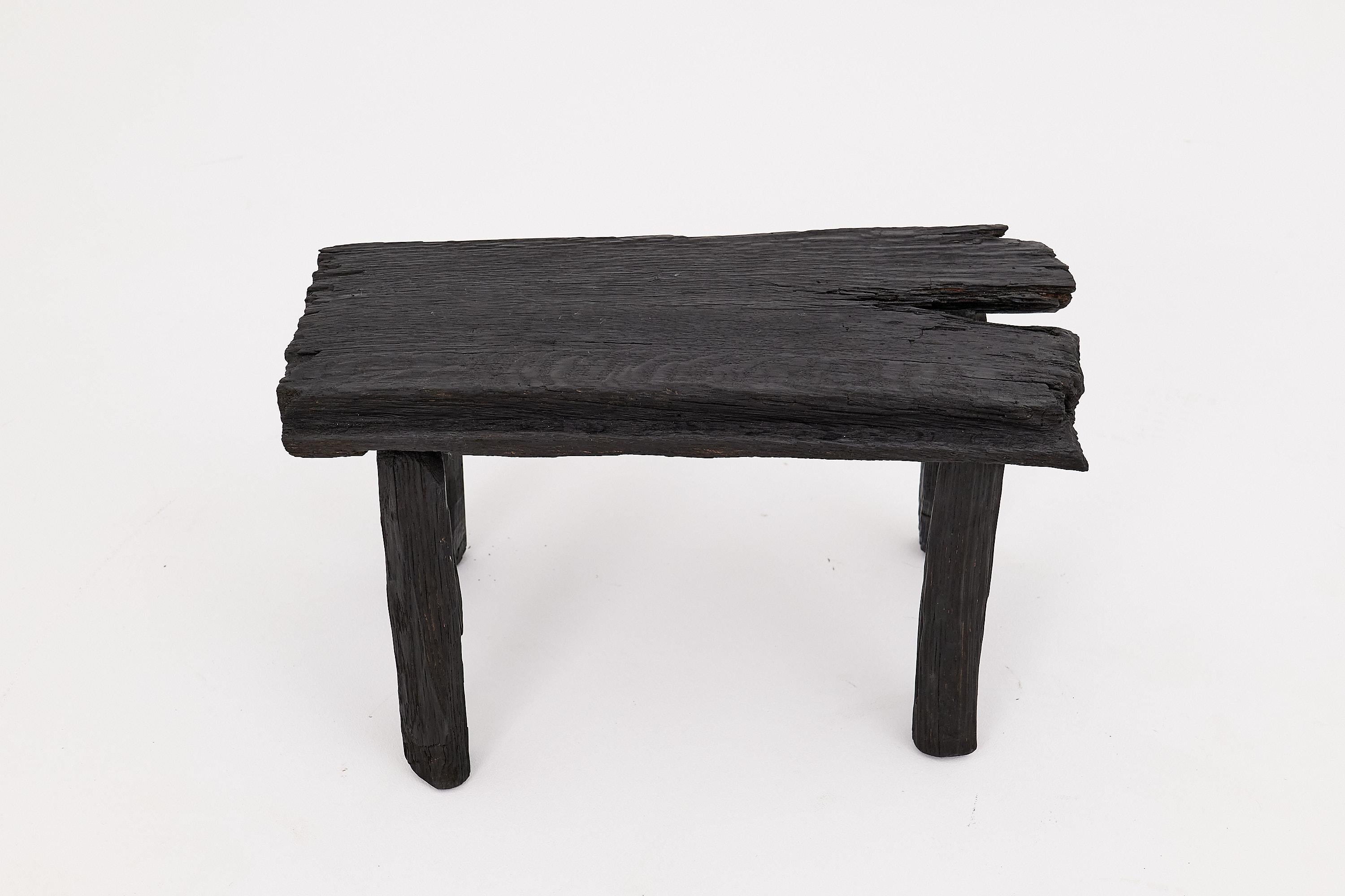 Ce tabouret sculptural en bois carbonisé capture l'essence de l'élégance primitive, fusionnant une texture brute avec une forme audacieuse et minimaliste. Sculpté à la main dans du bois dur massif récupéré, le tabouret présente une surface