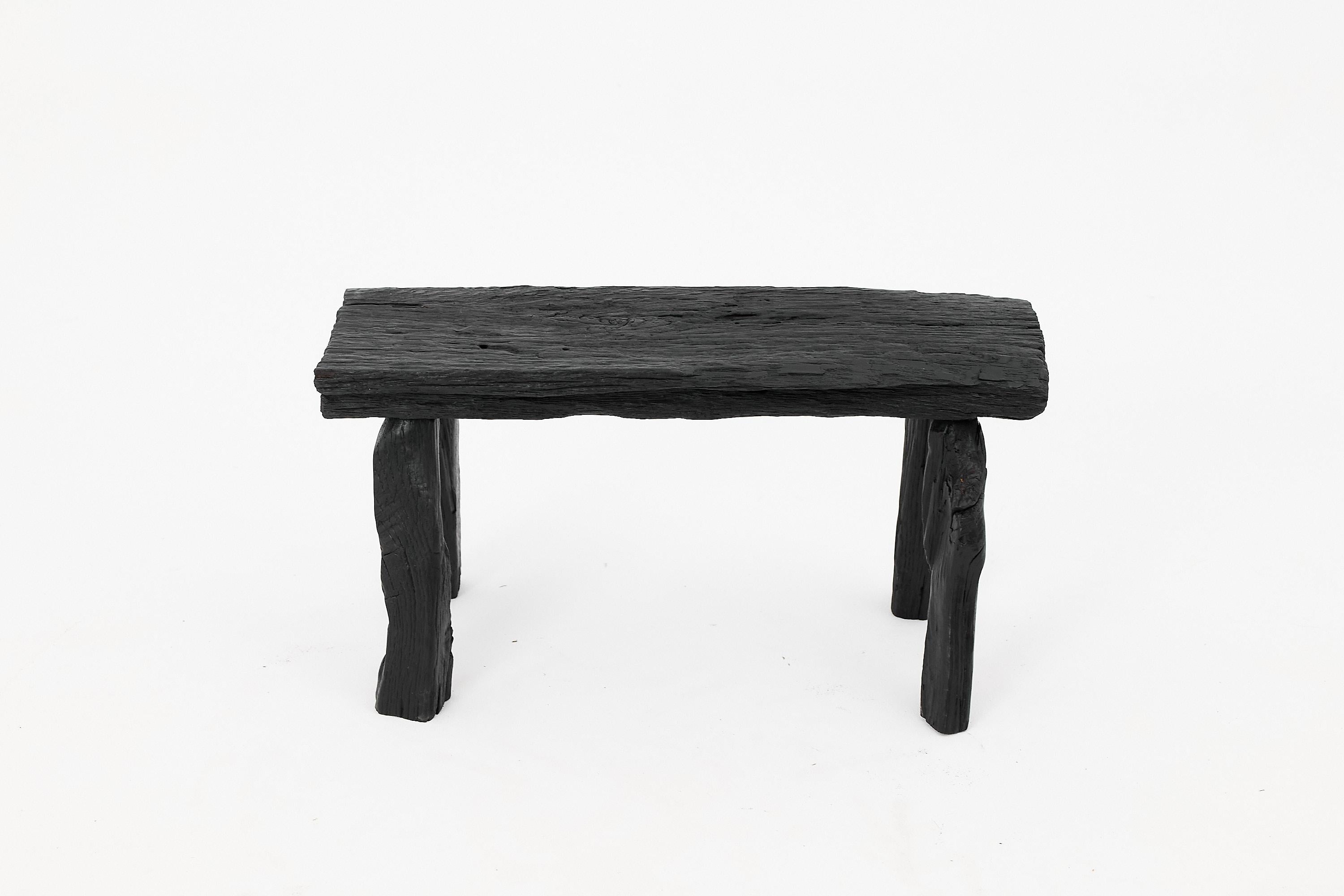 This sculptural charred wood stool captures the essence of primitive elegance, fusing raw texture with a bold, minimalist form. Hand-carved from solid reclaimed hardwood, the stool features a deeply blackened surface achieved through an intense