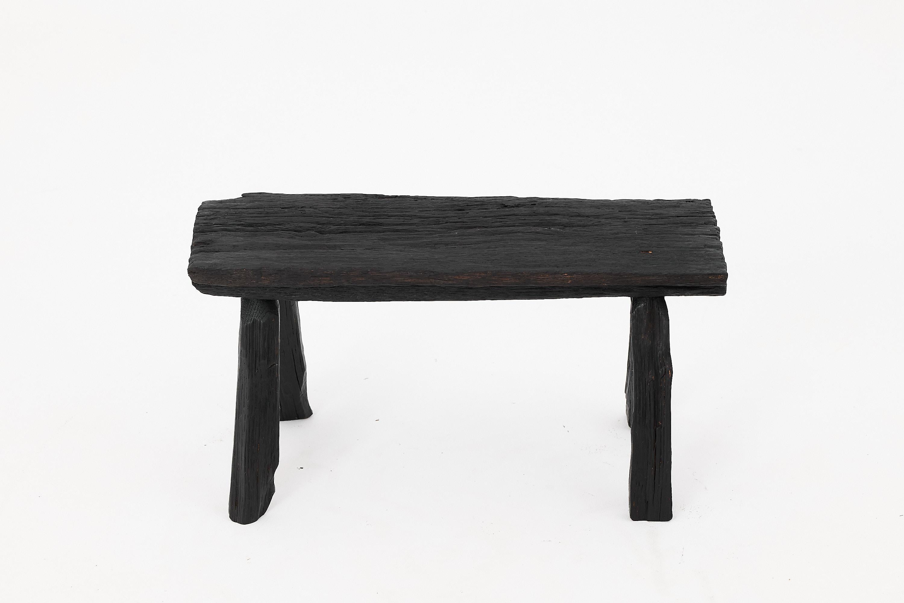 This sculptural charred wood stool captures the essence of primitive elegance, fusing raw texture with a bold, minimalist form. Hand-carved from solid reclaimed hardwood, the stool features a deeply blackened surface achieved through an intense