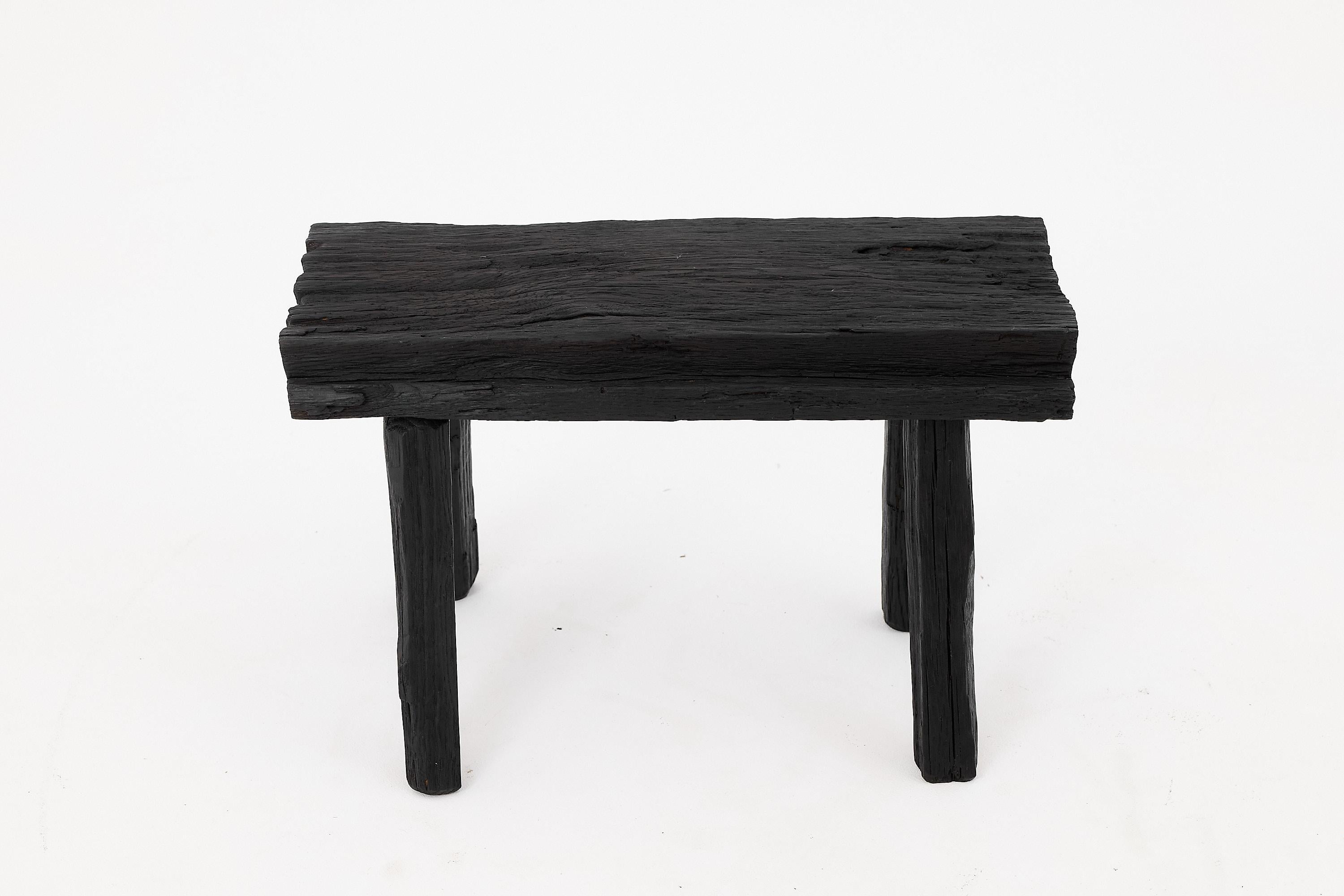 Questo sgabello scultoreo in legno carbonizzato cattura l'essenza dell'eleganza primitiva, fondendo la consistenza grezza con una forma audace e minimalista. Scolpito a mano da legno massiccio di recupero, lo sgabello presenta una superficie