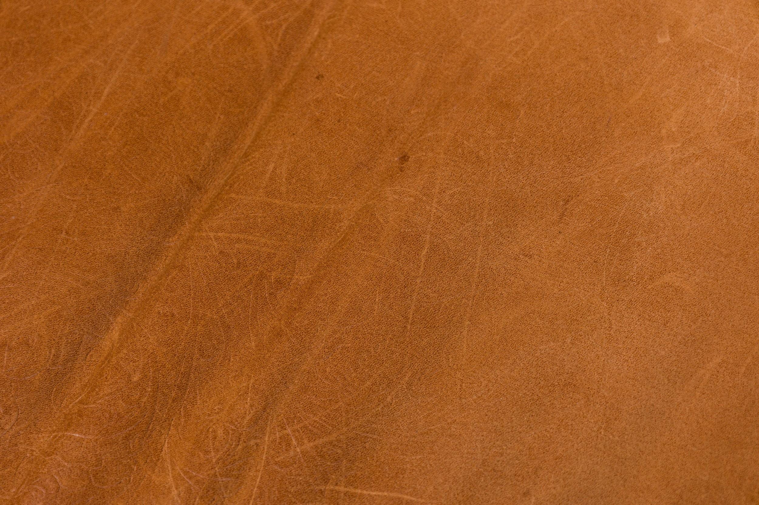 Fauteuil rustique de style Adirondack surdimensionné avec une structure en bois de racines blondes, un dossier en angle avec des lattes verticales en bois rond et un coussin d'assise et de dossier amovible en cuir brun caramel gaufré et fleuri.