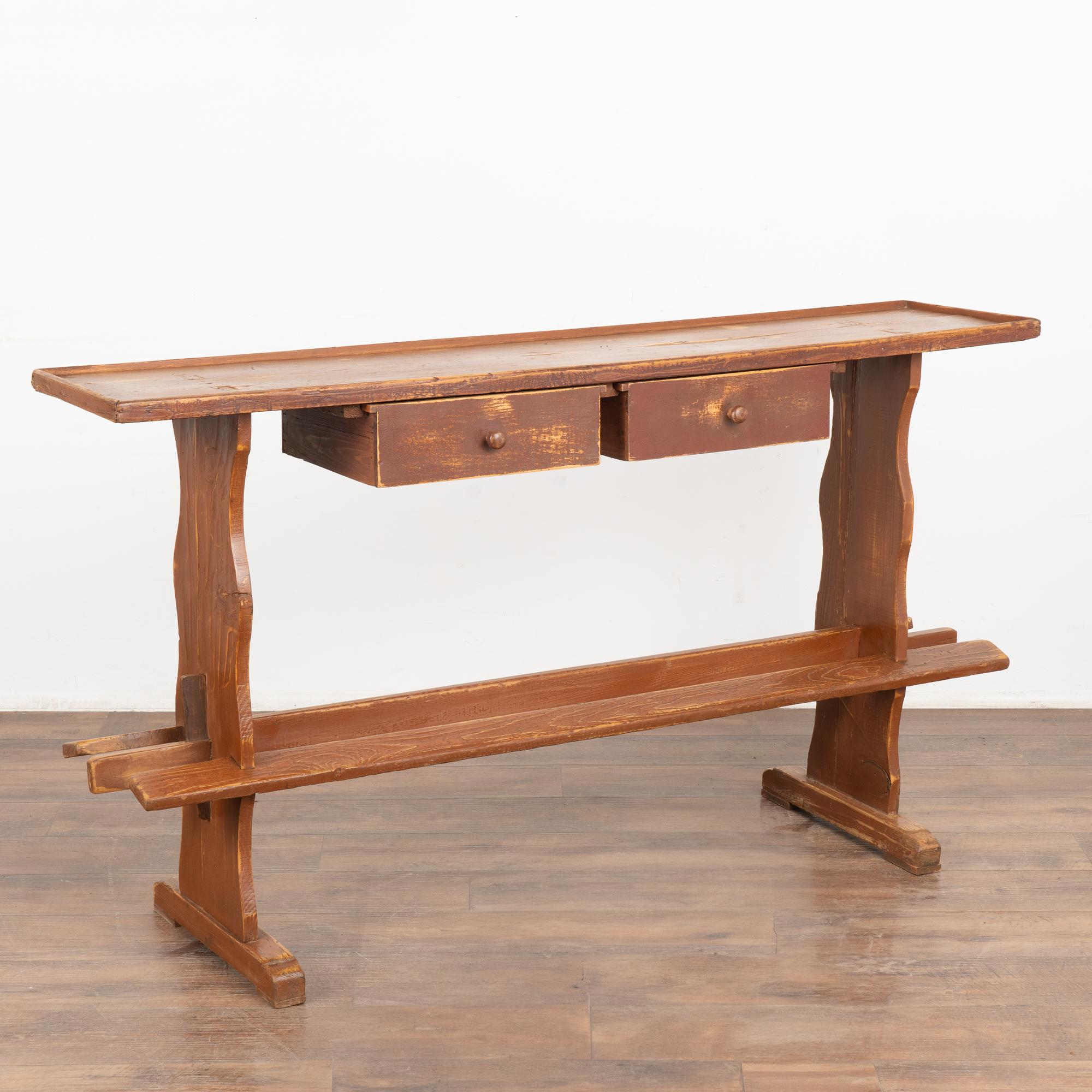 This narrow console table is both unique and charming, thanks to the gently distressed original brown paint, two drawers and trestle base adding to its rustic country appeal.
Note there is a trim or edge around the top.
This table has been restored,