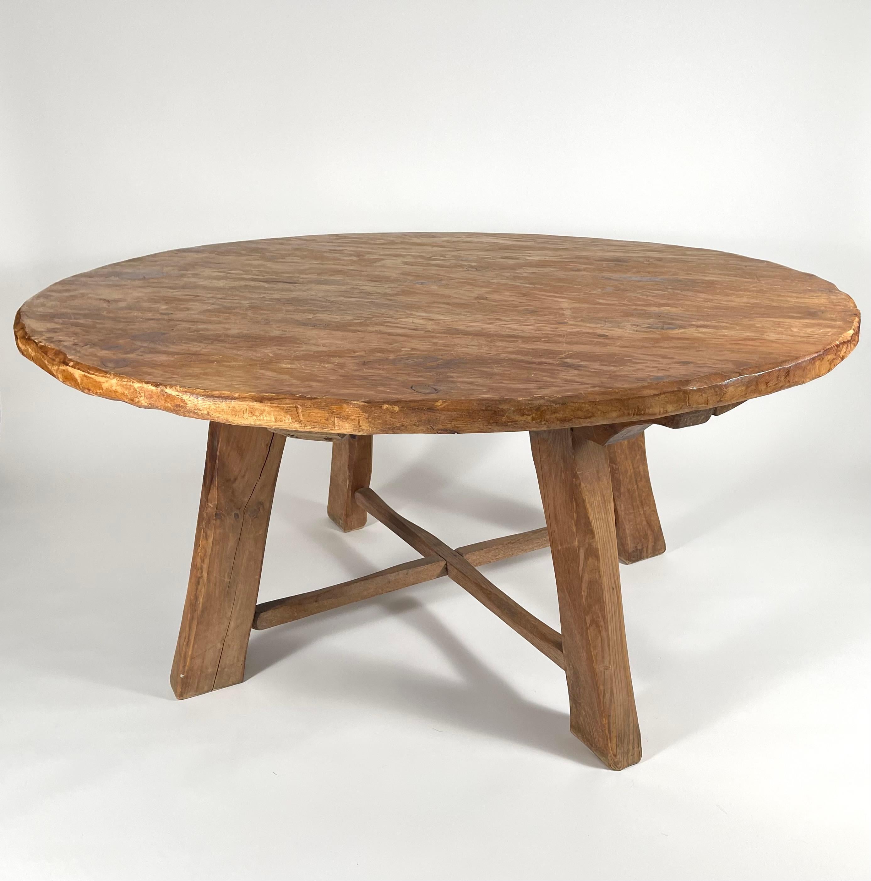 A pine round dining table with carved rusticated top and 4 heavy square section legs, chamfered and rusticated, joined by cross stretchers. Good, natural, surface. Comfortably seats 8. Very solid, with character and a strong form.