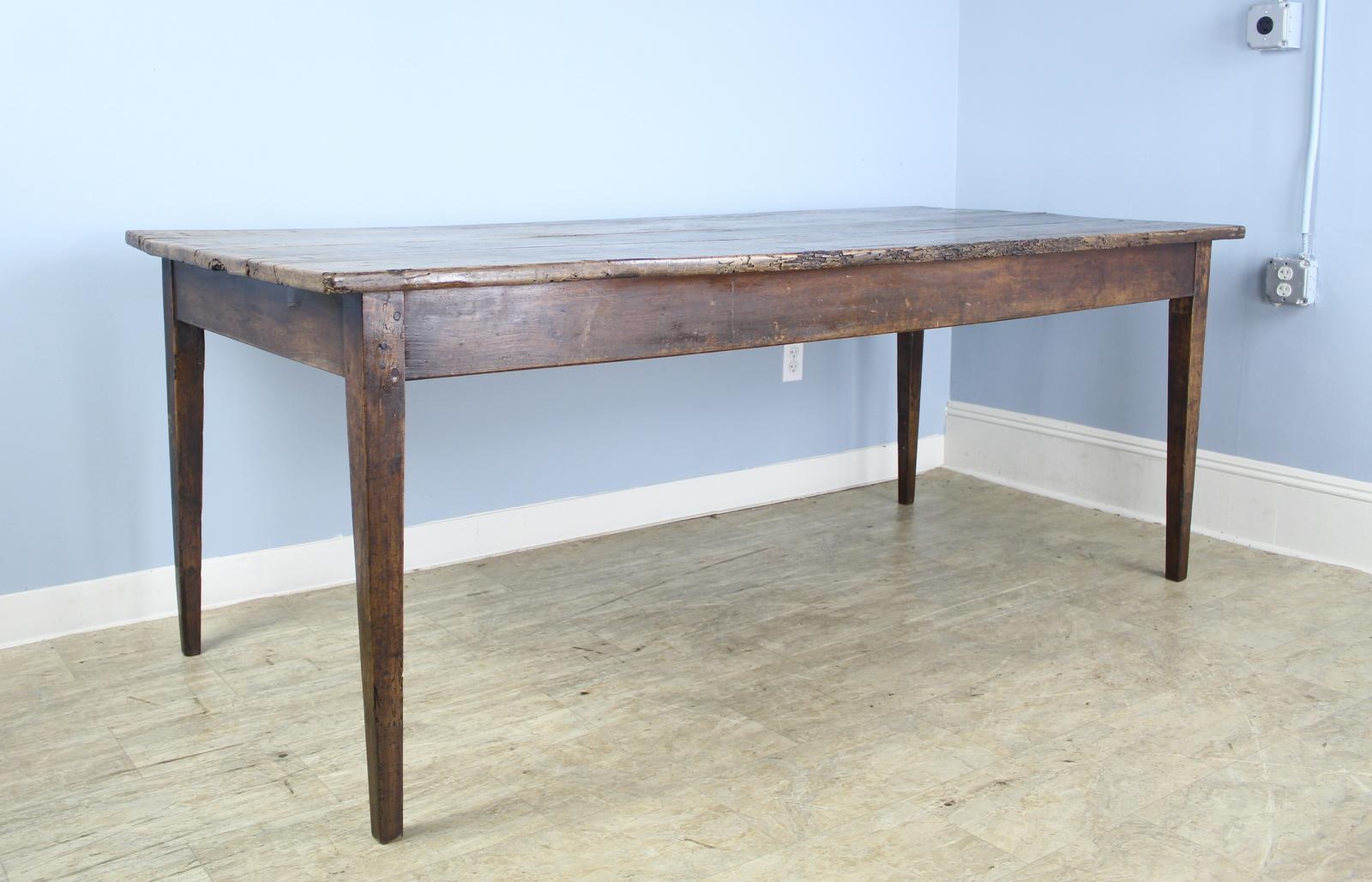 A classic cherry farm table, generously proportioned with unusually good depth for a table of this age. Nice tapered legs and mellow color. The top has dramatic original distress which adds a strong note of interest, shown in several of the
