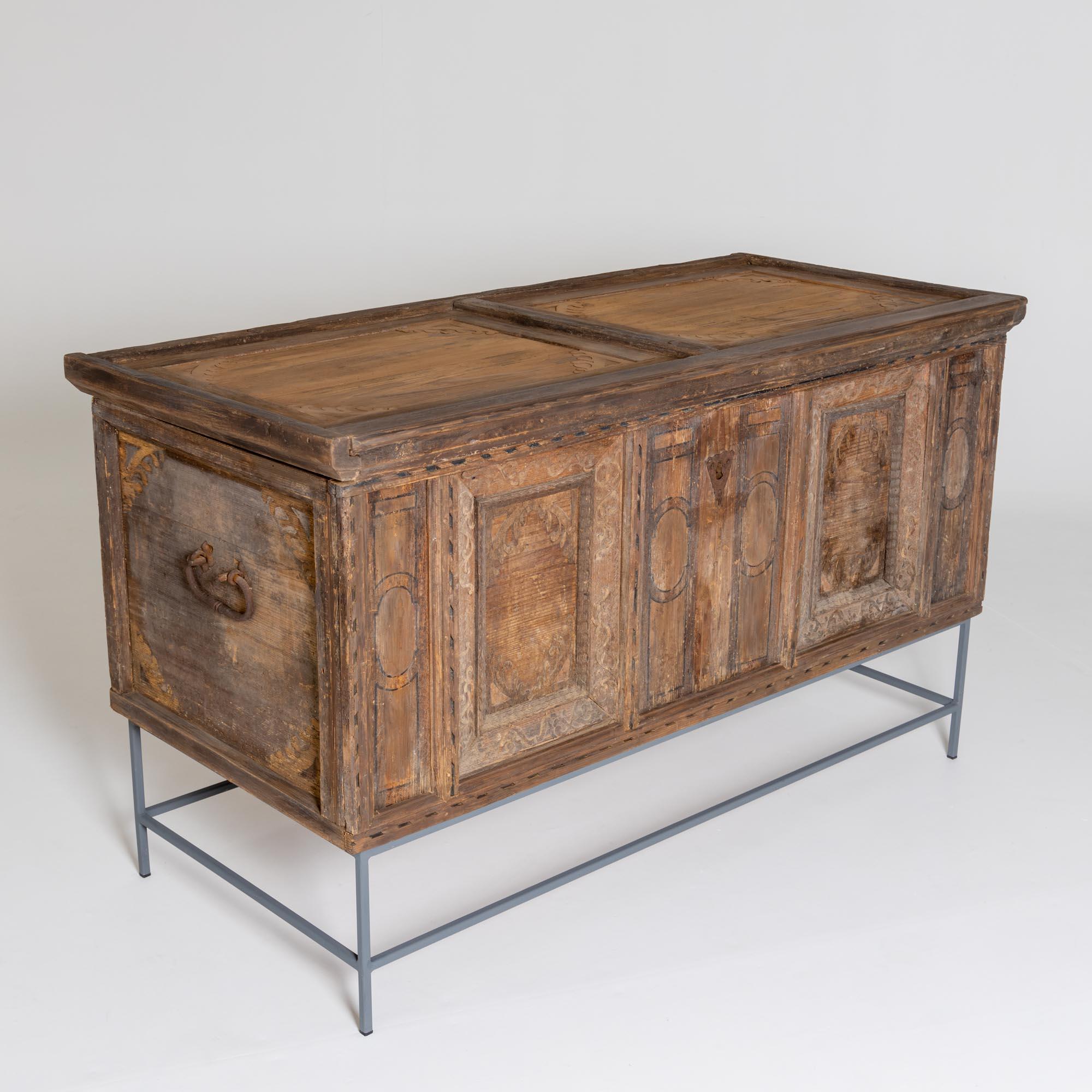 Flat-lidded chest made of softwood with side handles and iron fittings. The chest stands on a modern metal frame (height: 31 cm). The chest is partly painted and partly decorated with applied vine decorations.