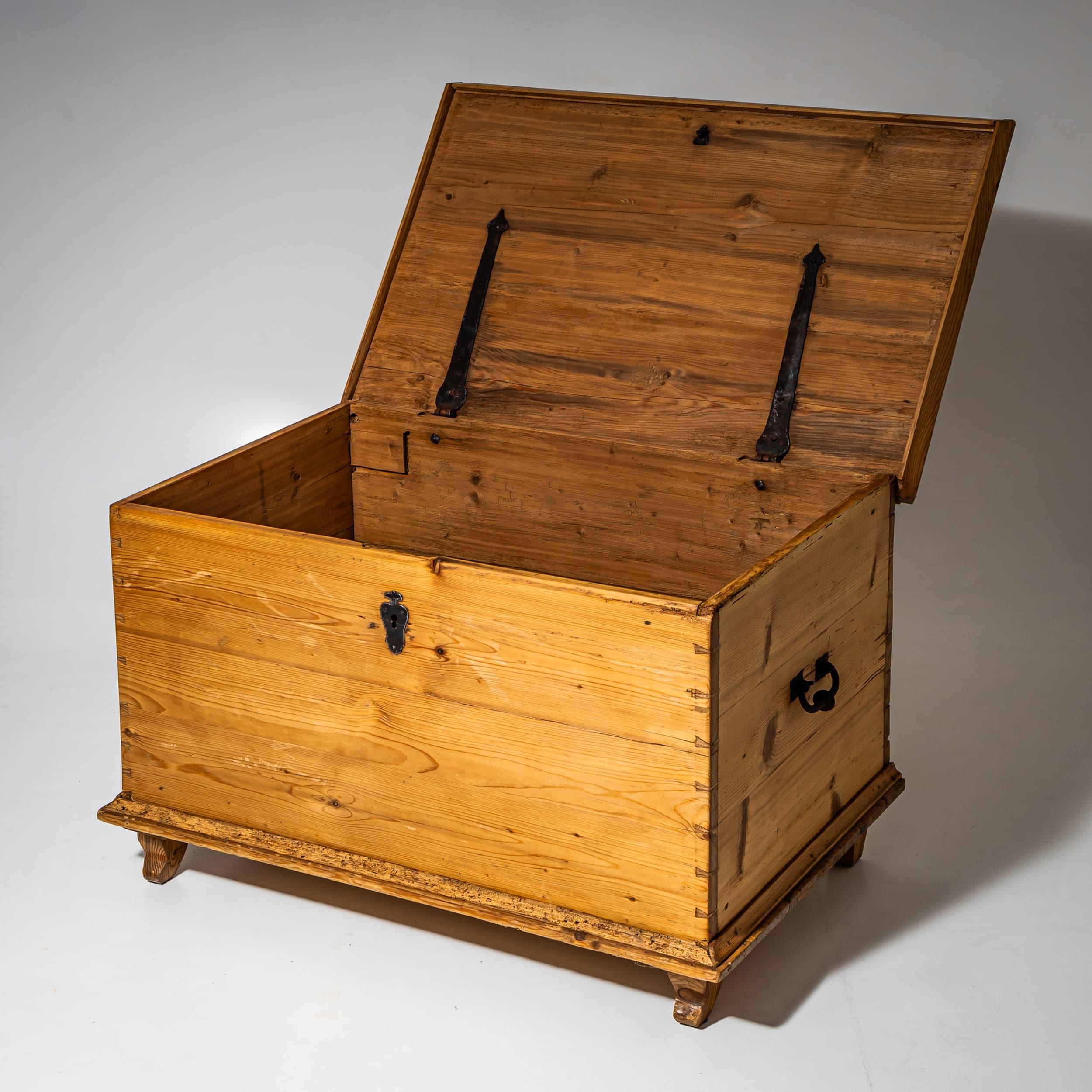 Cassapanca rettangolare semplice realizzata in legno di abete massiccio, con piedi a blocco leggermente strombati e una modanatura alla base. La parte anteriore e i lati sono costituiti da tavole unite orizzontalmente, con un coperchio liscio e