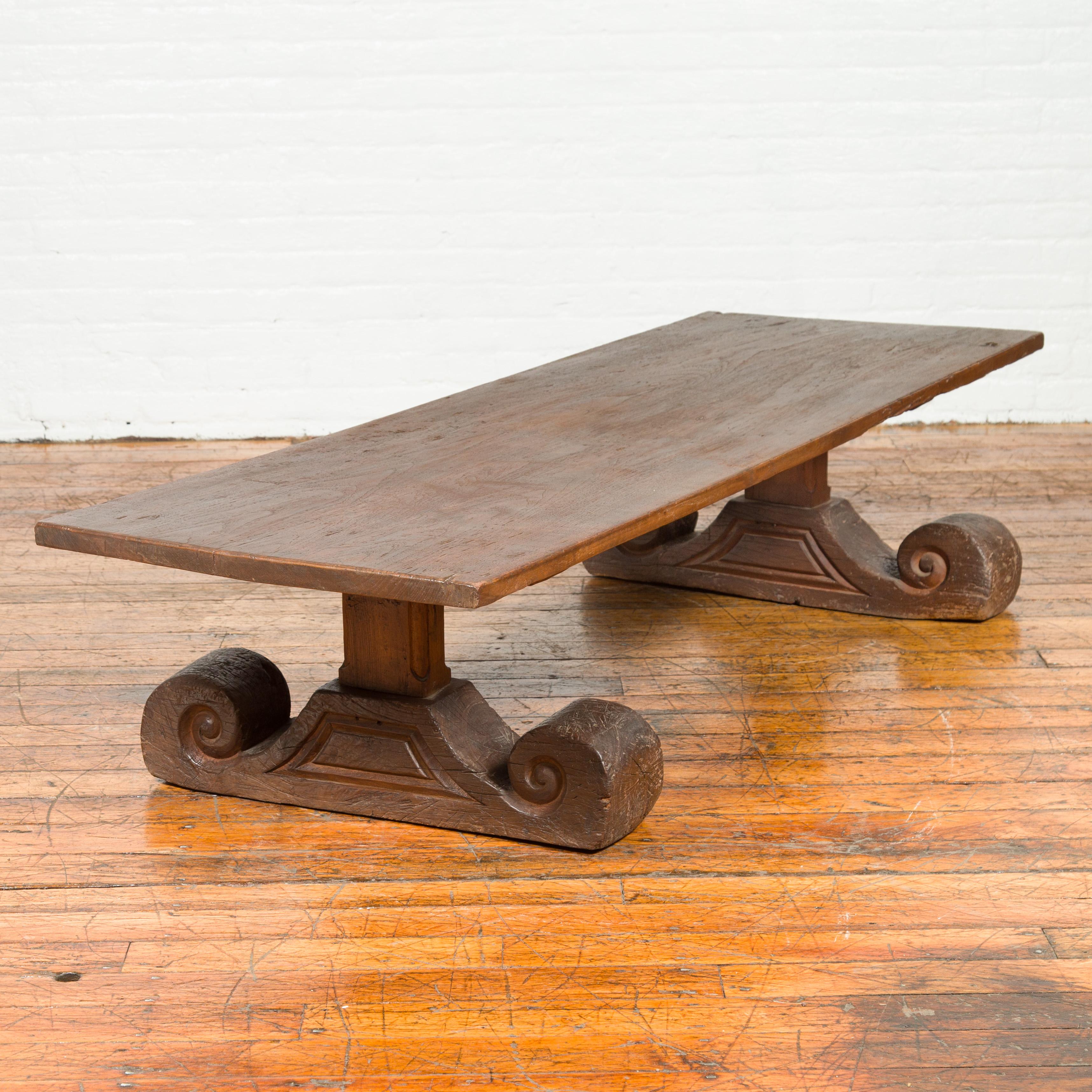 An antique Chinese elmwood coffee table from the 19th century, with scrolling base. Born in China during the 19th century, this rustic yet elegant coffee table features a rectangular top sitting above a base that catches our attention with its large