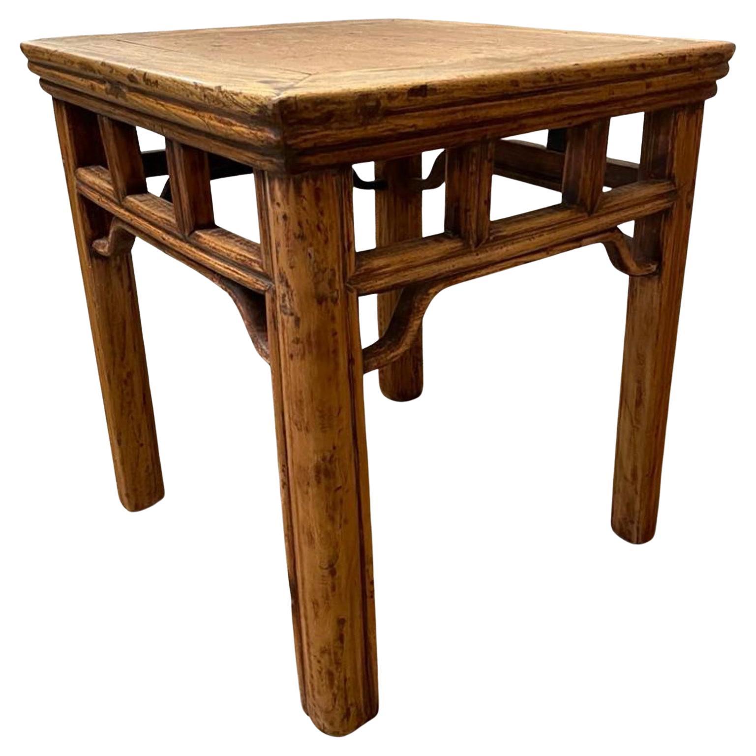 A rustic country Chinese Qing dynasty style elmwood side table from the early 20th century, with pierced pillar-shaped struts apron. This Chinese end table features a square top with central board and beveled edges. Originally conceived to be a