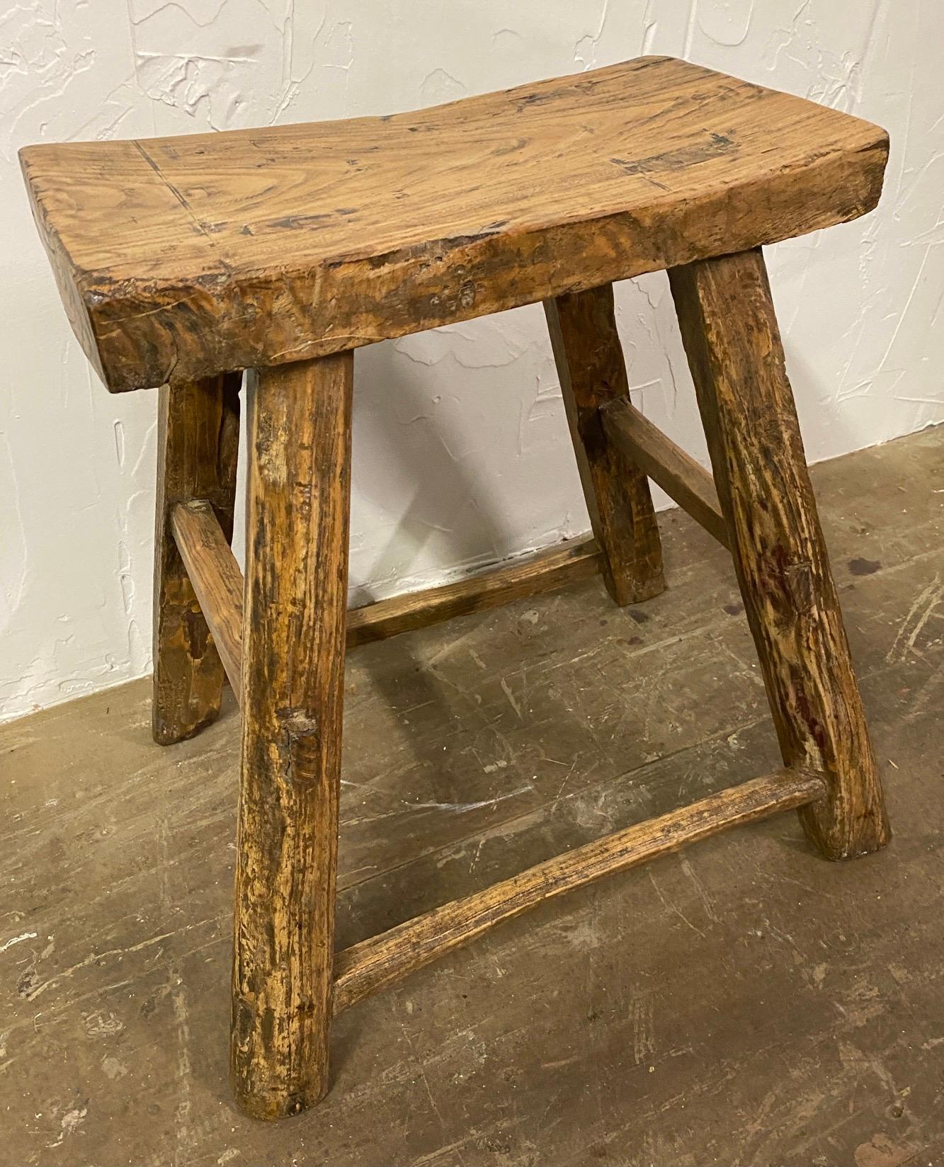 Dated to the early 20th century, this rustic stool has simple splayed-leg design and well-worn finish. Crafted of northern elm wood with mortise-and-tenon joinery, without the use of nails or screws, the stool features a rectangular seat and four