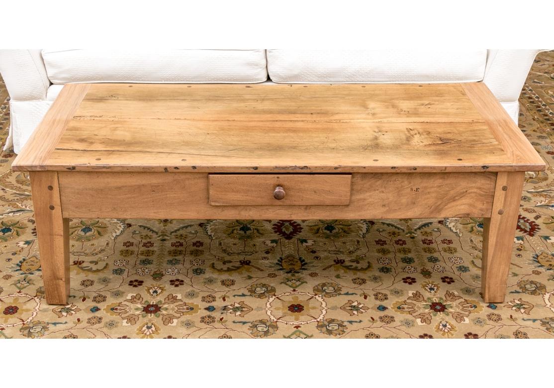A very well made and sturdy Cocktail Table with peg construction and a planked breadboard top with a wide apron resting on thick tapered square legs. There is one central drawer with a simple turned knob. The table is set off by nicely figured wood