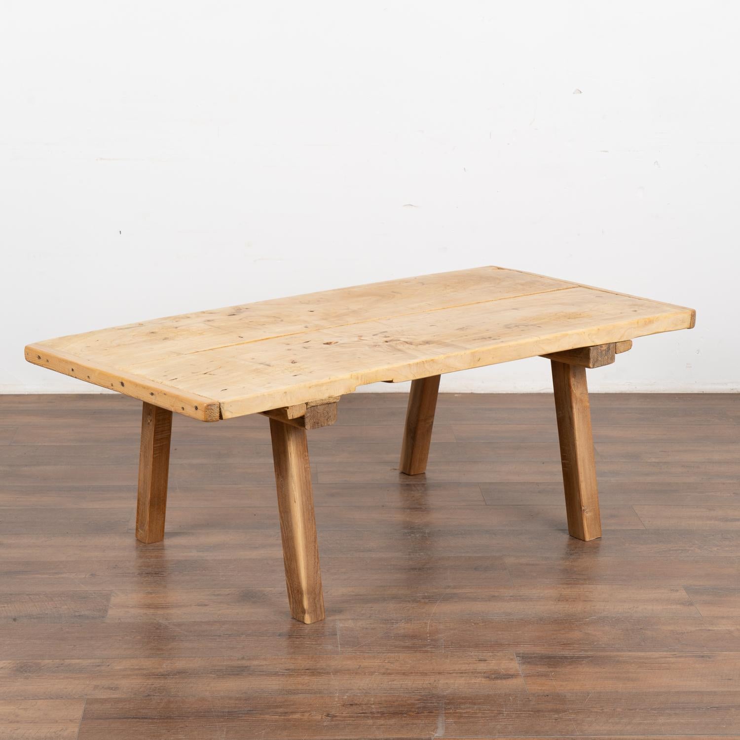 The appeal of this coffee table comes from the rustic wood top that originally served as a work table and rests on original peg legs. 
Note the scratches, nicks, gouges, stains, aged separation of wood and old cracks that all combine to build the