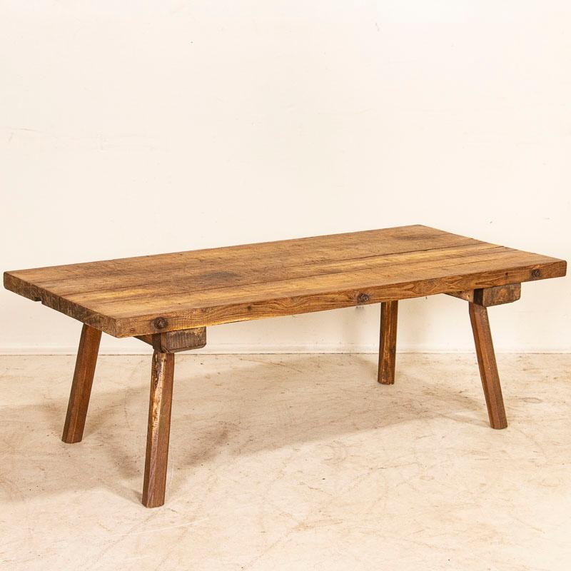 The weathered wood of this rustic coffee table has been heavily distressed, indicating the thick top served as a work table in its early life due to the many gouges and scrapes found in it. Originally it possibly served in a butcher's shop as